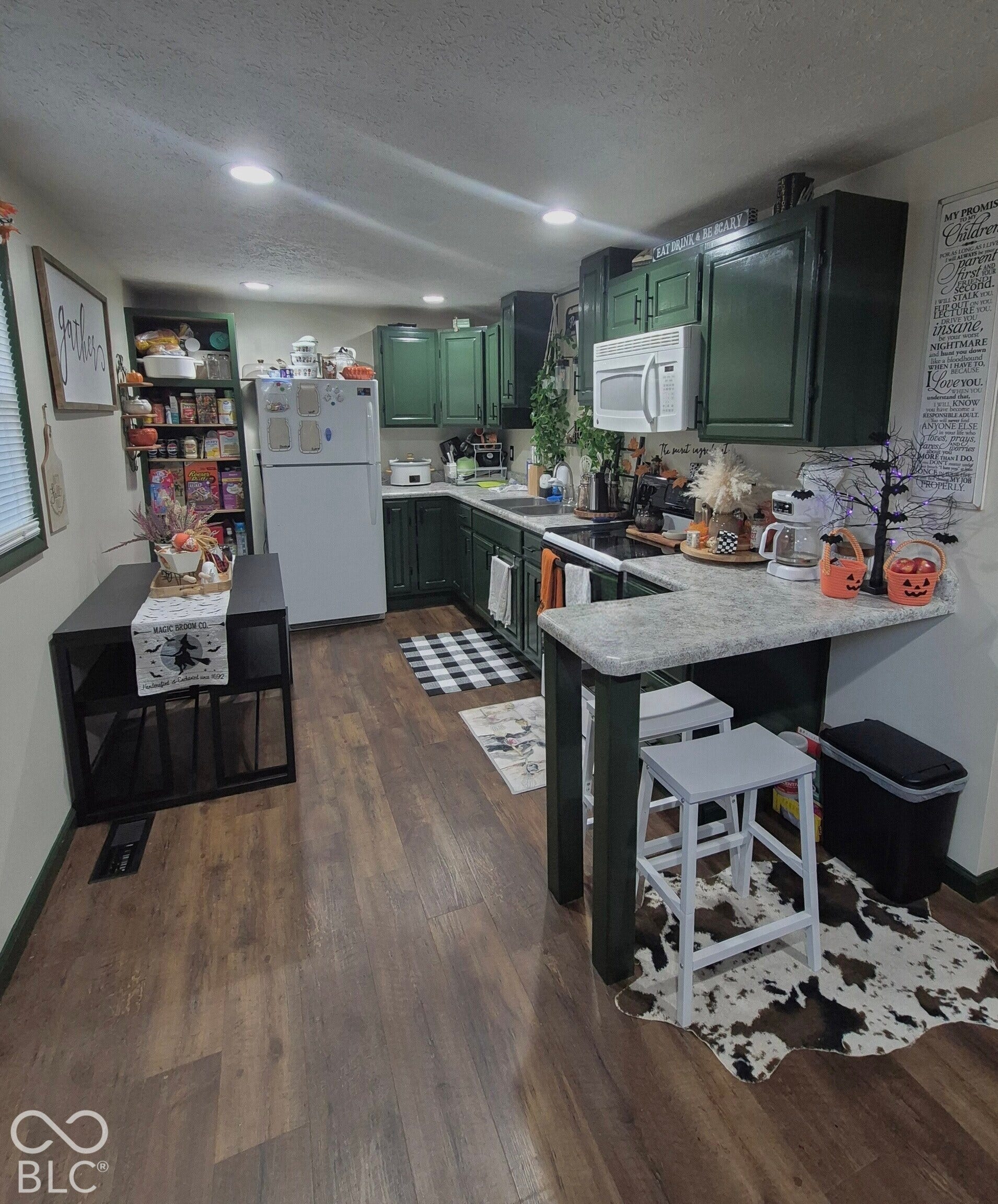 Kitchen featuring dark green cabinetry, white appliances, wood-finish flooring, recessed lighting, and a breakfast bar with a light-toned countertop
