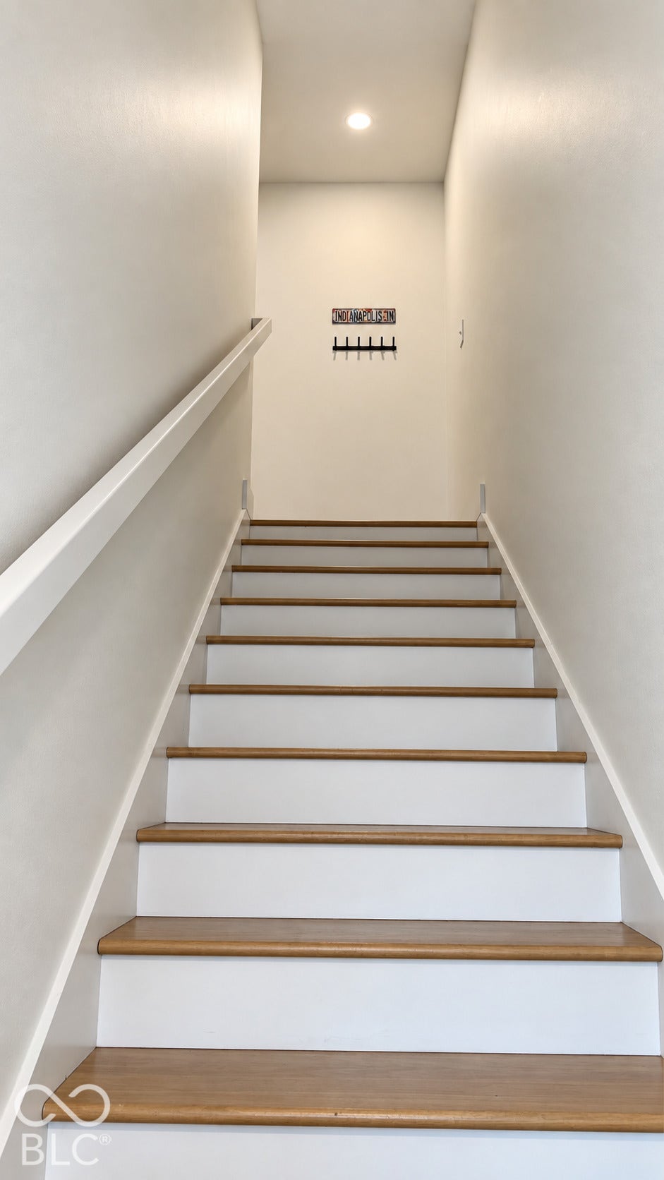 Staircase featuring wood-finish treads, white risers, and a white handrail