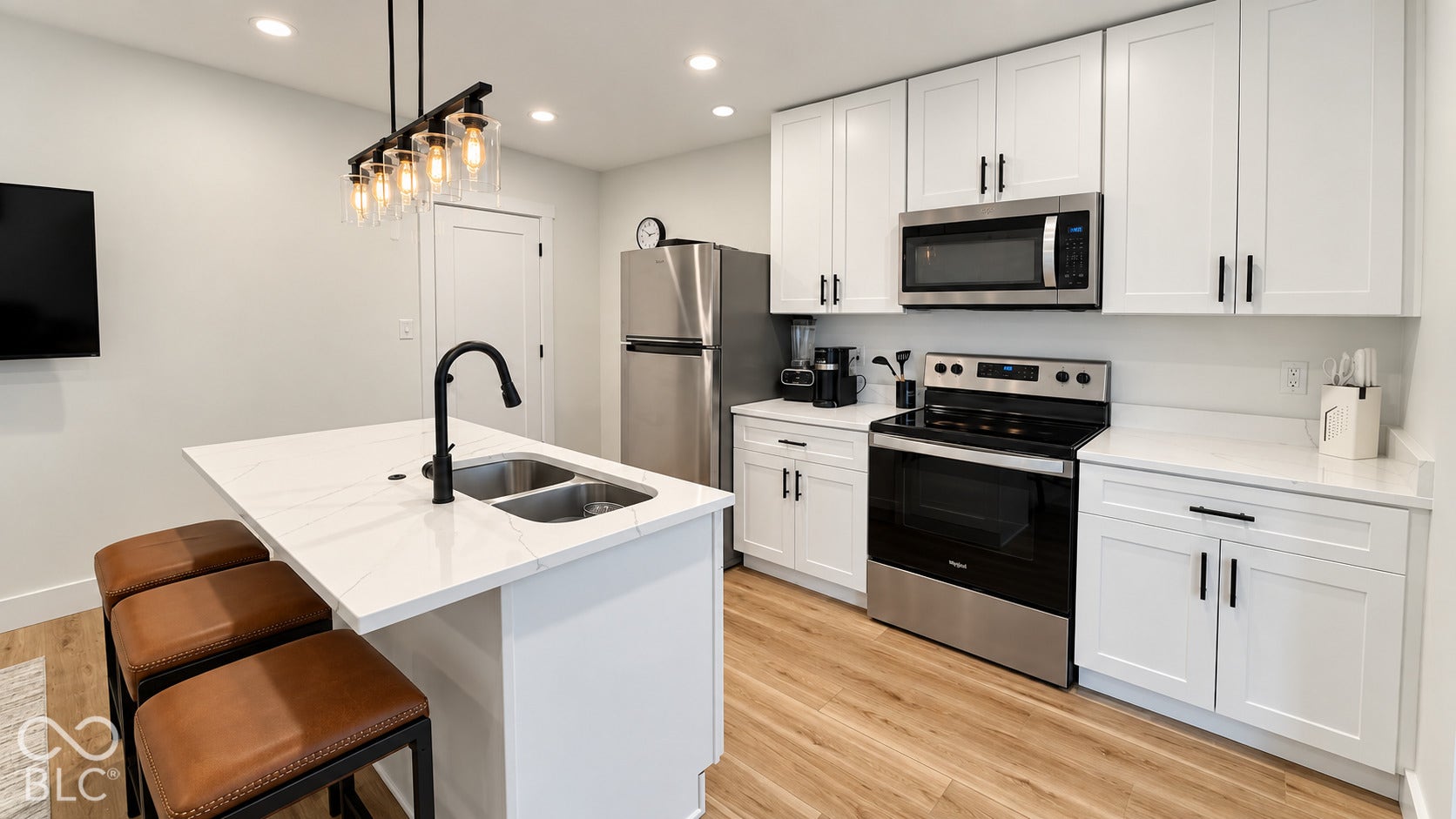 White shaker cabinetry with black hardware, stainless steel appliances, wood-finish flooring, recessed lighting, and a kitchen island with an undermount sink