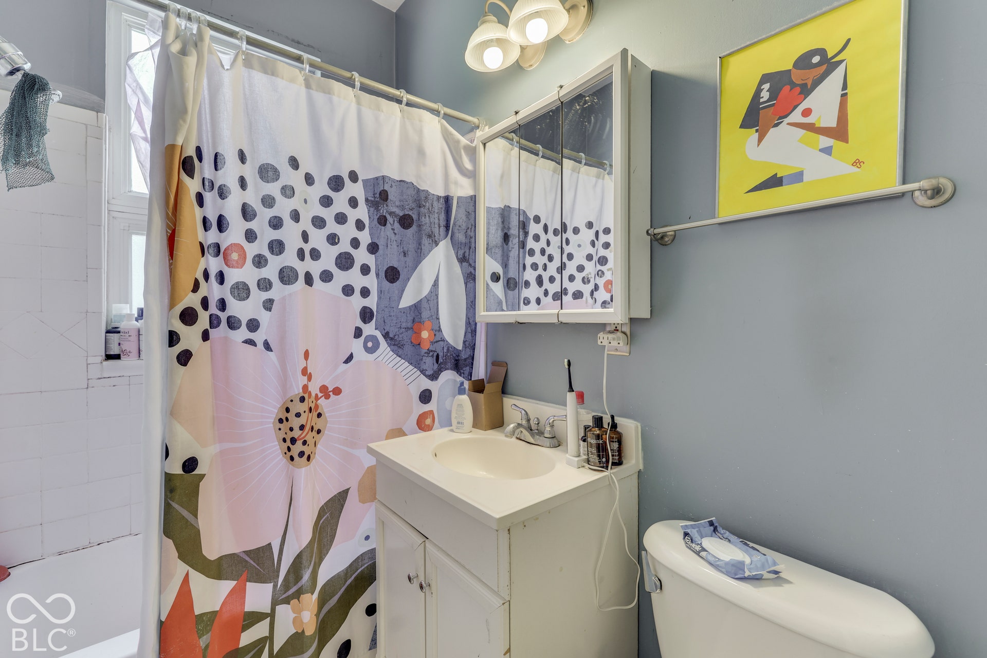 Unit 2 White vanity with integrated sink and chrome faucet, medicine cabinet with mirrored doors, wall-mounted light fixture, and blue painted walls