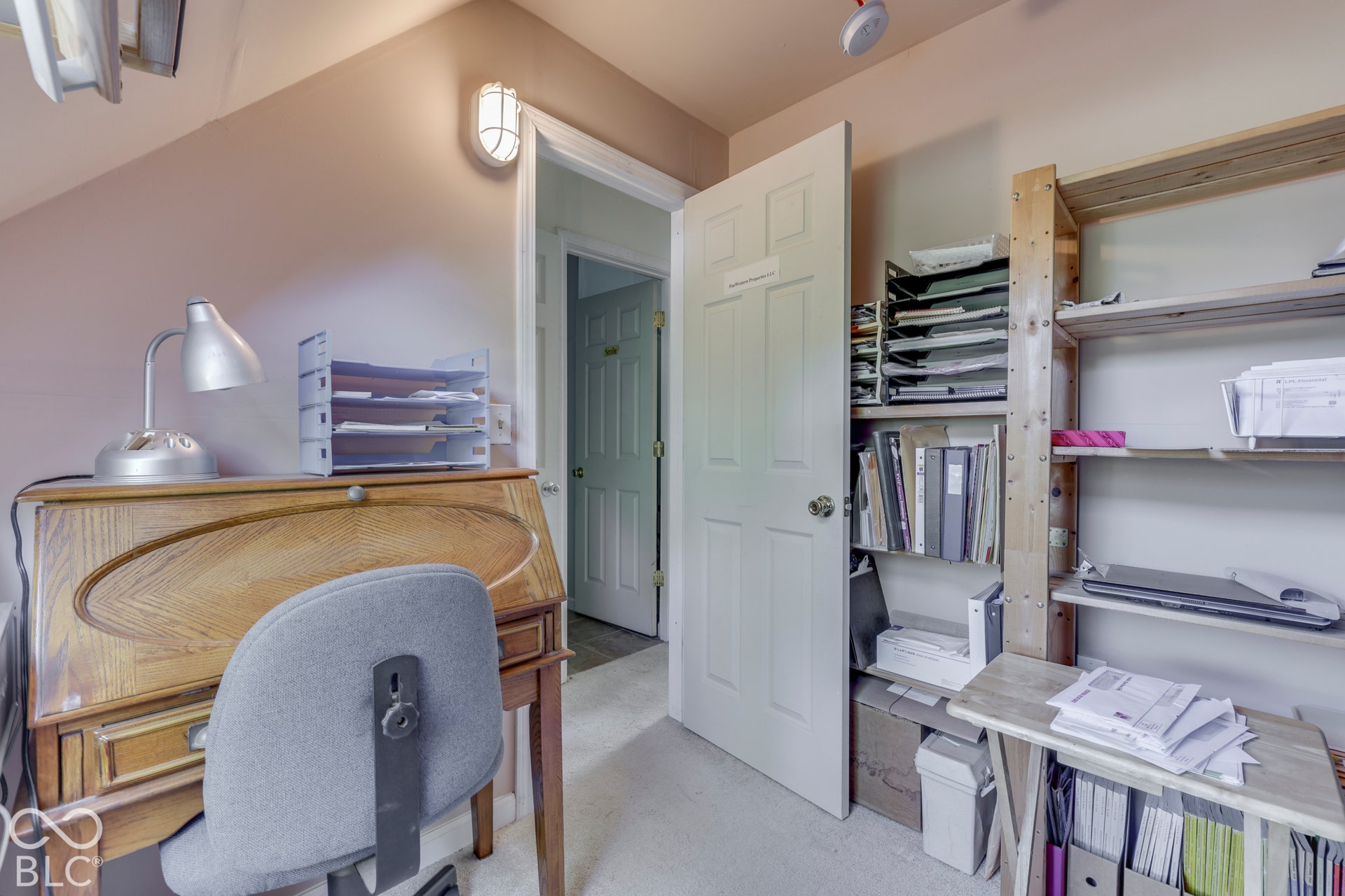 The office in the attic has carpeted flooring and built-in shelving.