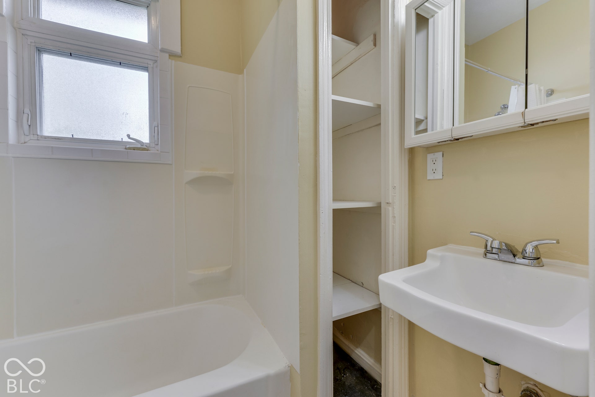Unit 3 Tub/shower combination with integrated shelving, wall-mounted sink, built-in storage shelving, and medicine cabinet with mirrored doors