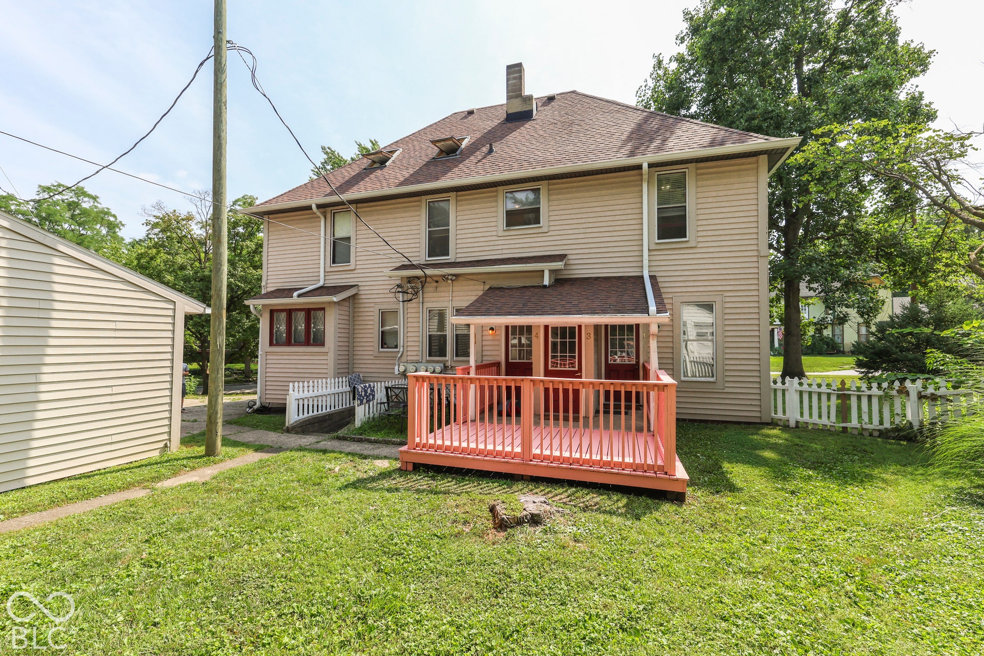 Large backyard featuring a large wood-plank deck with railing, a detached single-car garage, and a picket fence