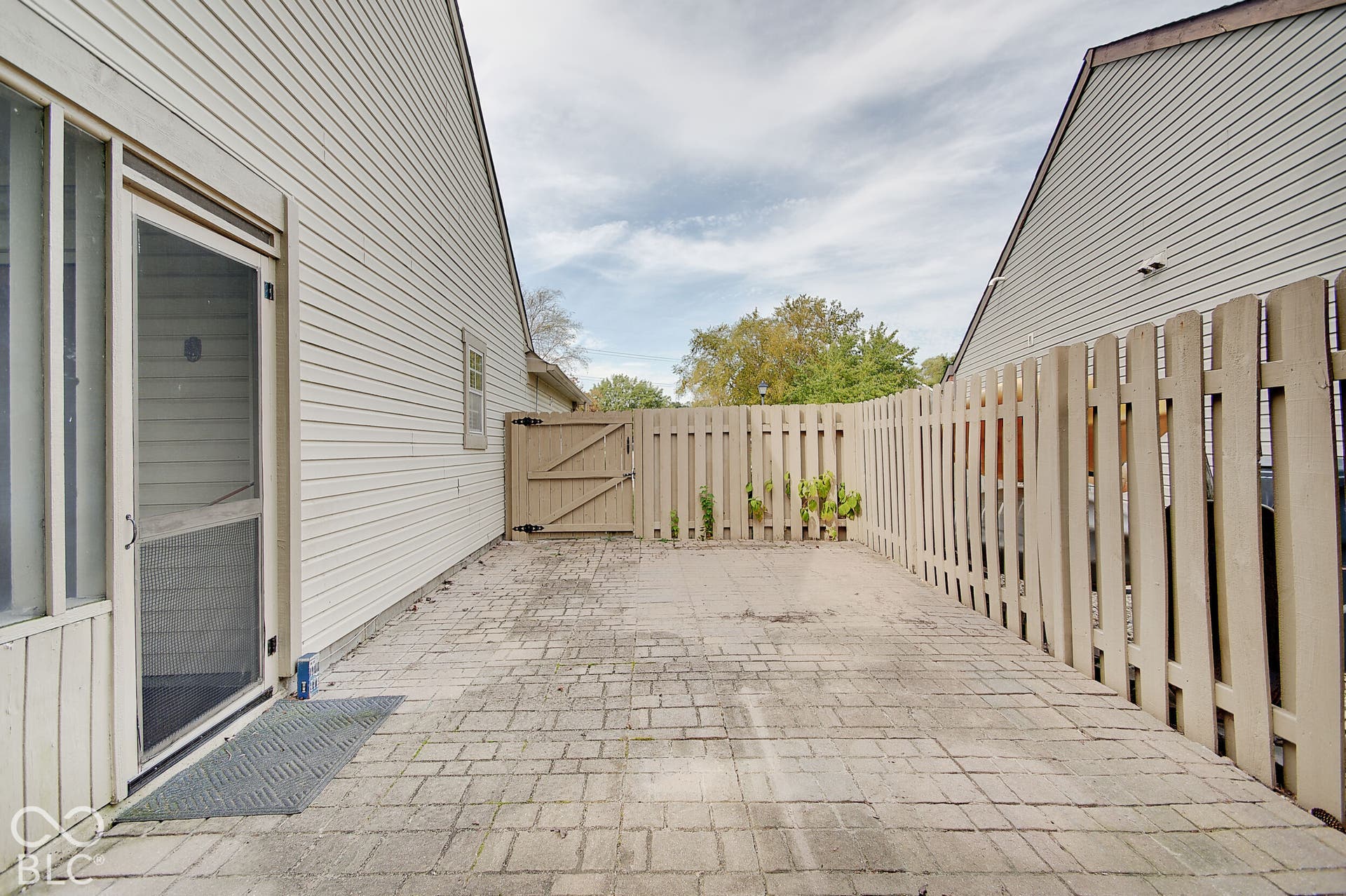 Paved patio area, privacy fencing, side gate access, and a screened door entry