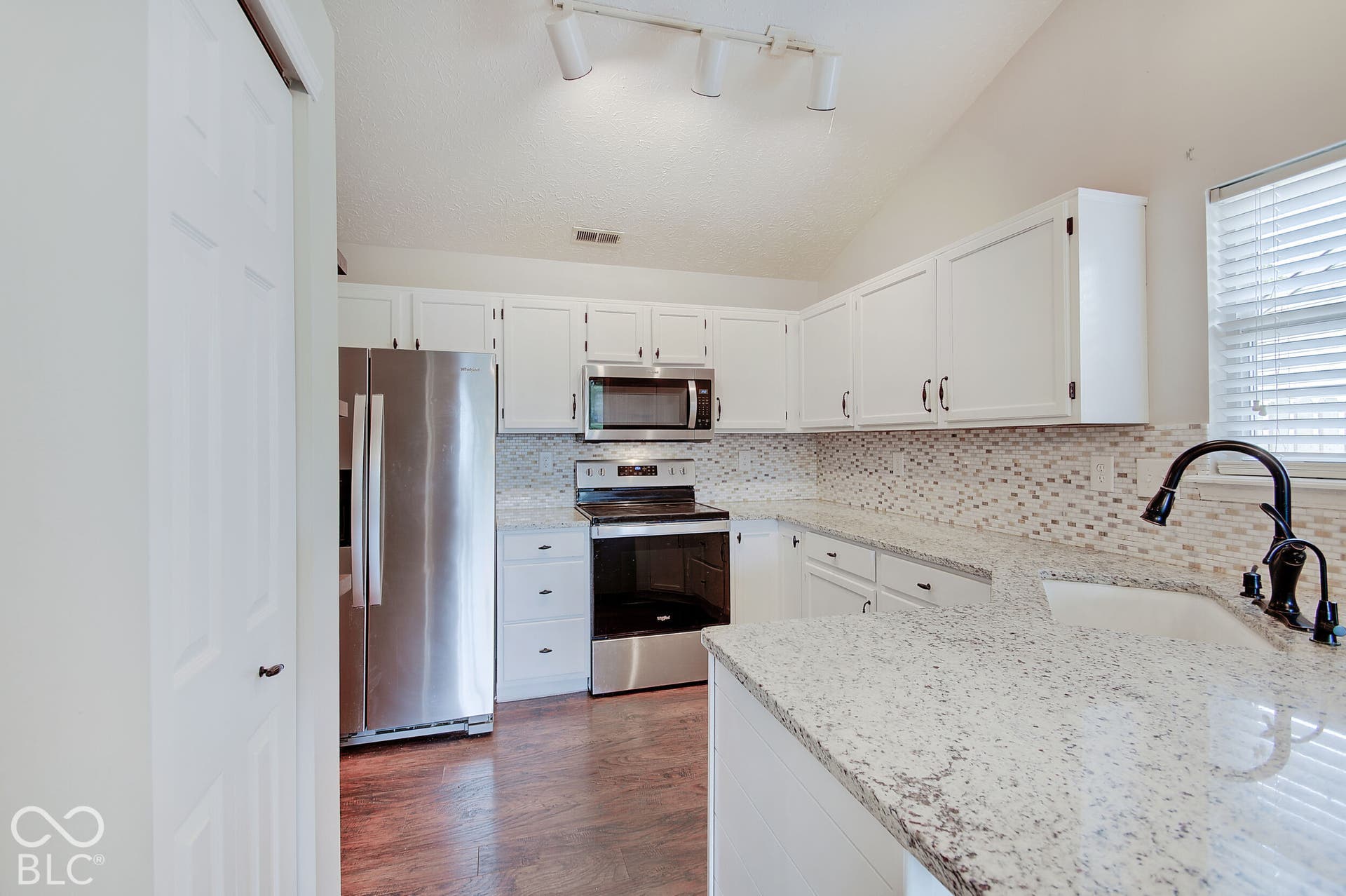 Kitchen featuring white cabinetry, stainless steel appliances, speckled countertops, and a mosaic tile backsplash