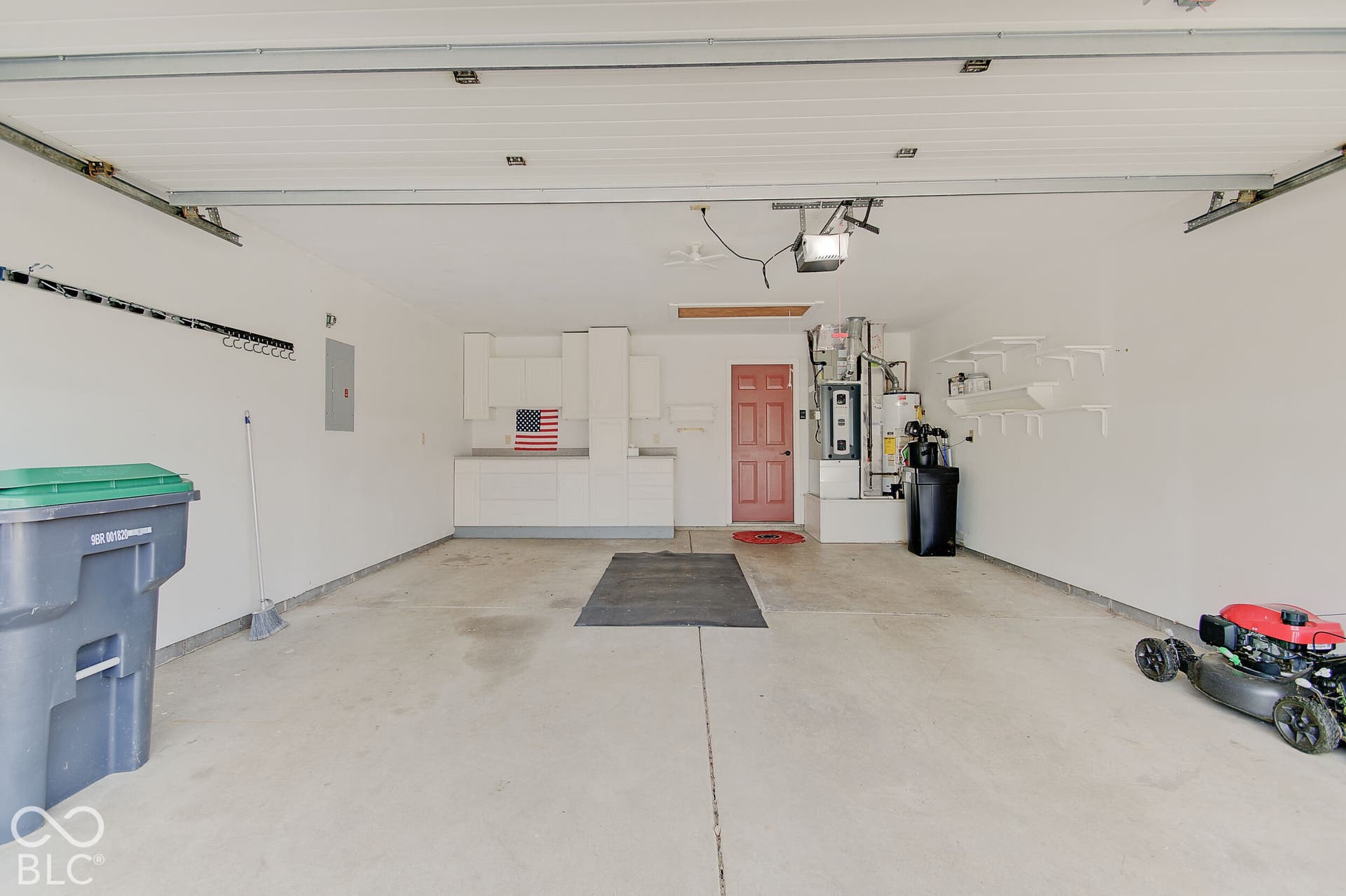 Attached two-car garage featuring a concrete floor, built-in white cabinetry, a red utility door, and a wall-mounted electrical panel