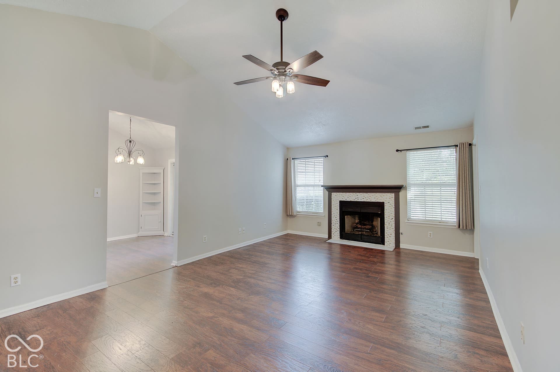 Vaulted ceiling, wood-finish flooring, ceiling fan with integrated lighting, fireplace with tile surround and wood mantel, built-in shelving in the adjacent room