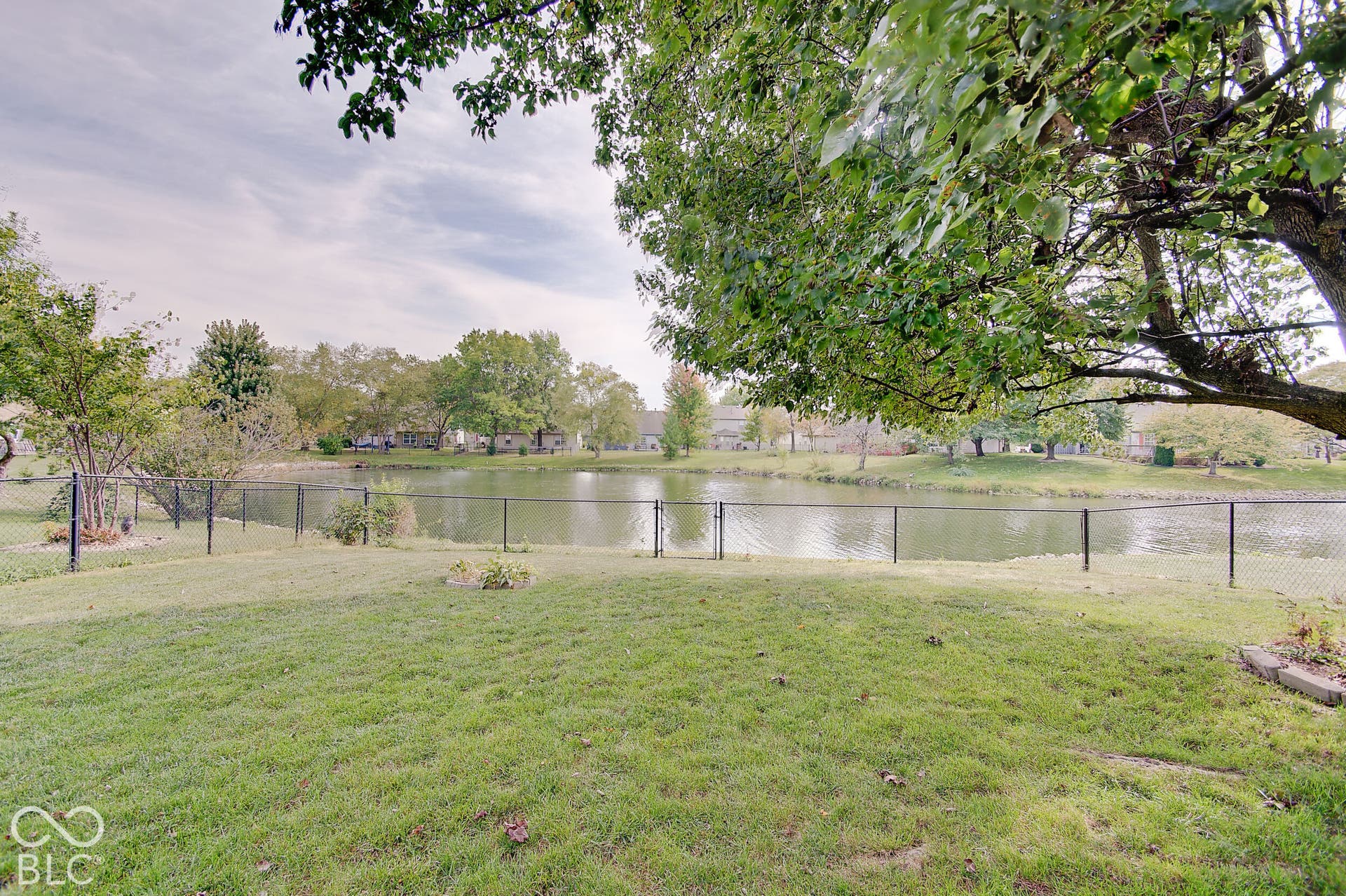 Expansive lawn with a chain-link fence, mature trees, and a visible body of water