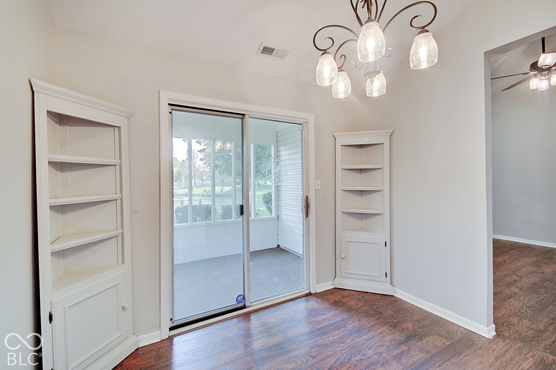 Wood-finish flooring, built-in corner shelving, sliding glass door to screened patio, and a decorative ceiling light fixture