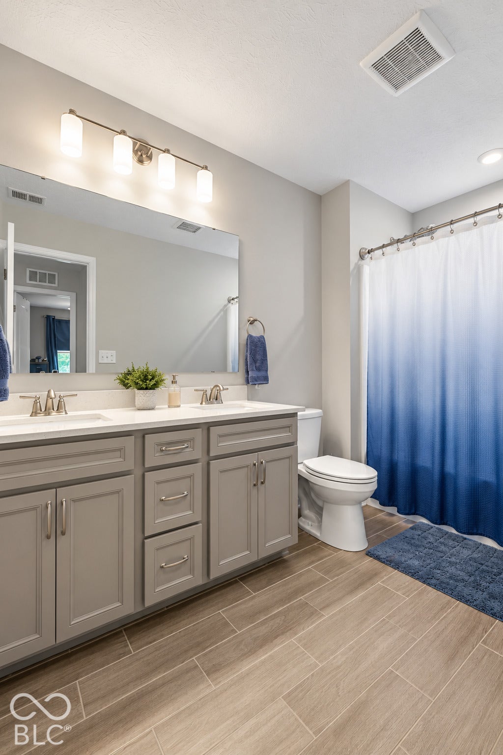 Dual vanity with gray shaker cabinetry, wood-finish tile flooring, recessed lighting, and a brushed nickel light fixture