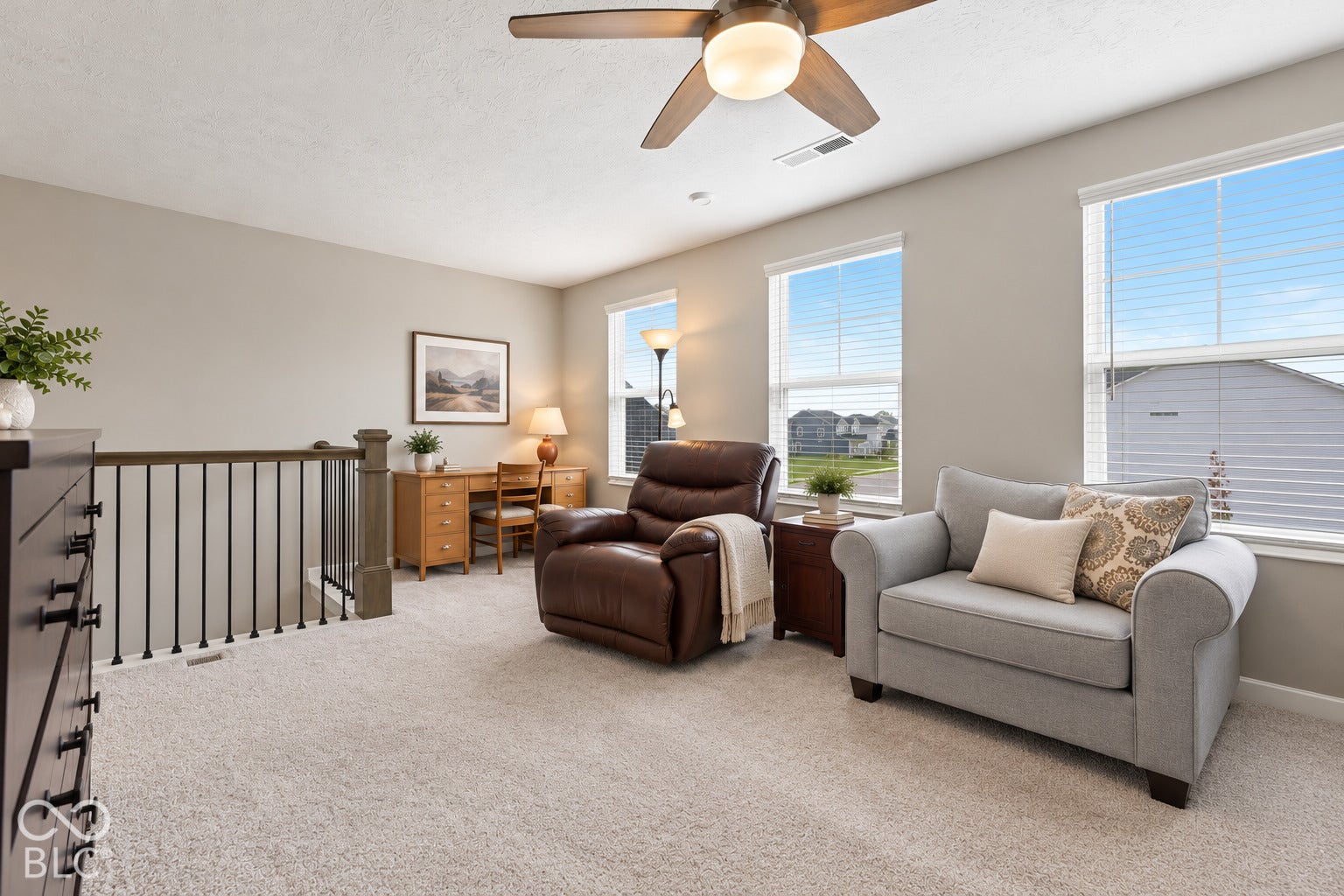Carpeted loft area featuring a ceiling fan, multiple windows with blinds, and a built-in railing
