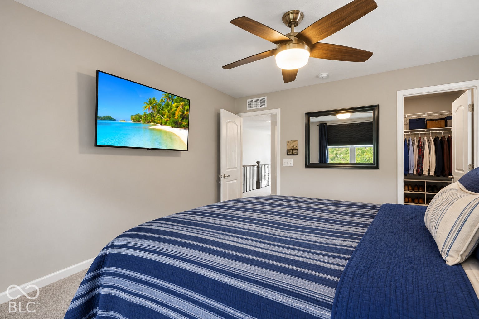 Wall-mounted television, ceiling fan with light fixture, large framed mirror, and an open closet with custom shelving