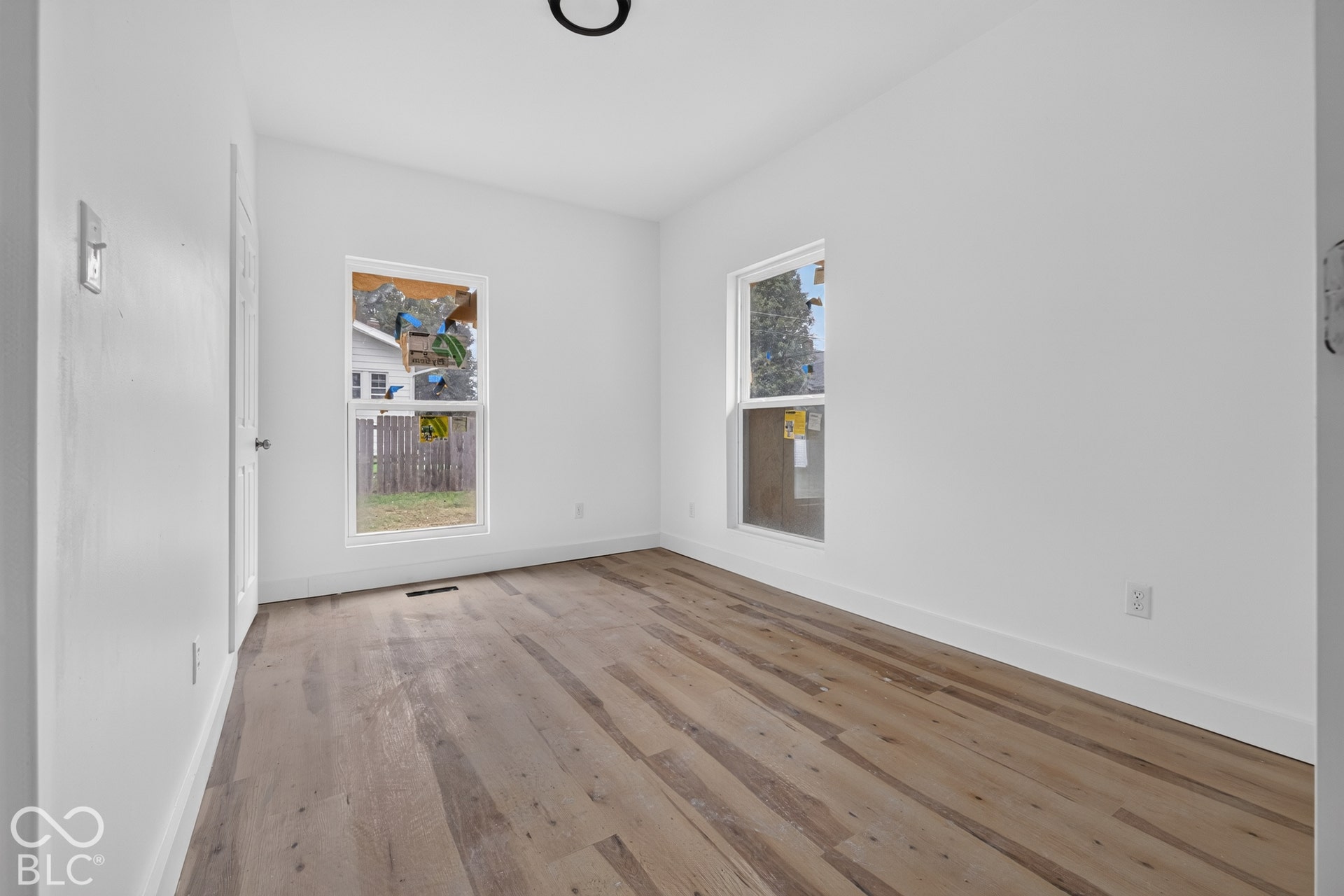 Wood-finish flooring throughout, white walls, two windows, recessed lighting, and a white interior door