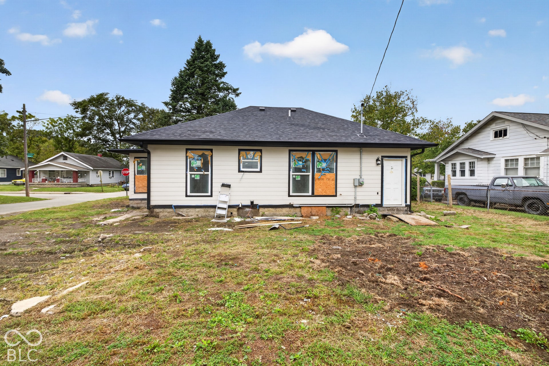 Light-toned horizontal siding with black trim, black shingle roof, and a white rear door