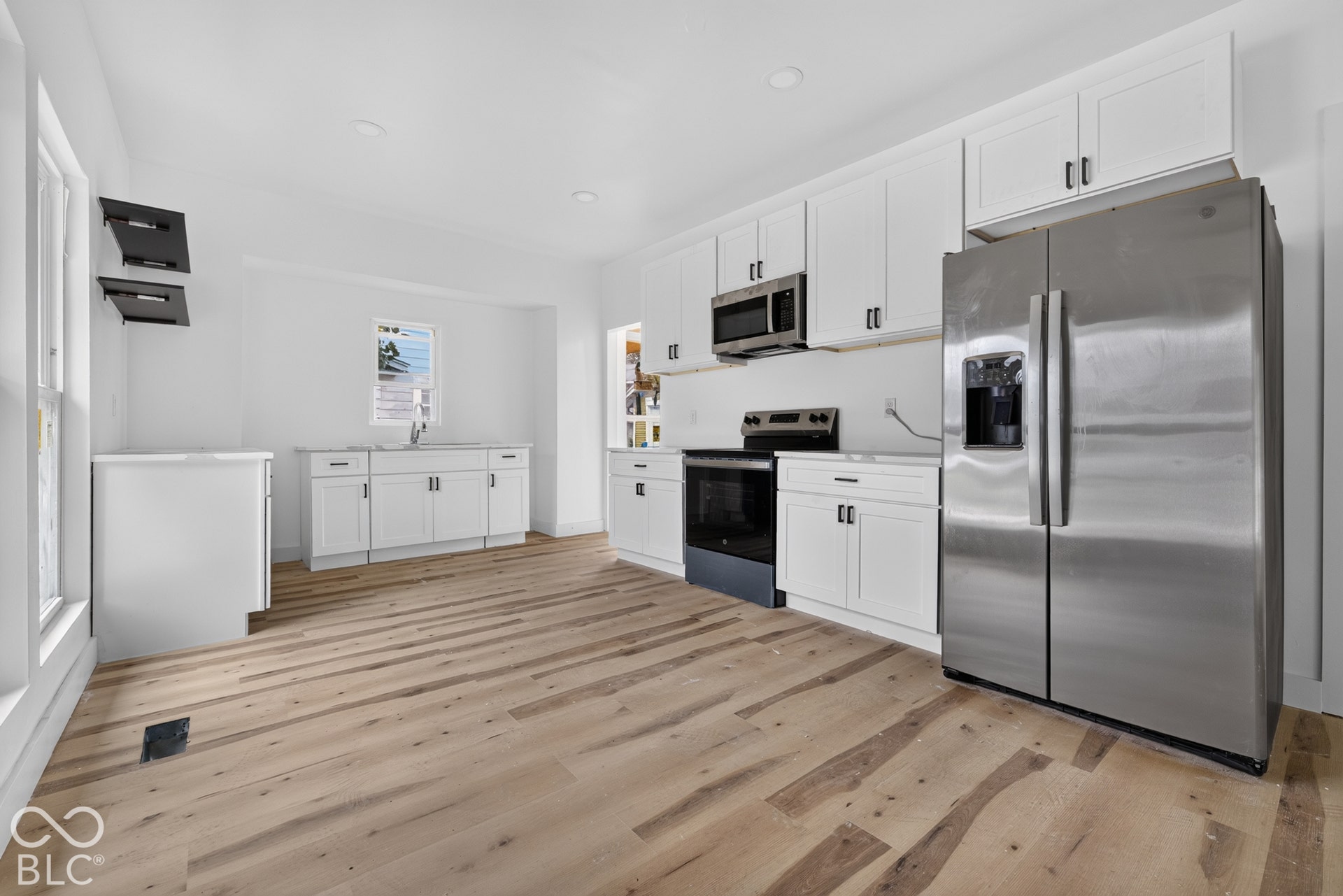 White shaker cabinetry with black hardware, stainless steel appliances, wood-finish flooring, and recessed lighting