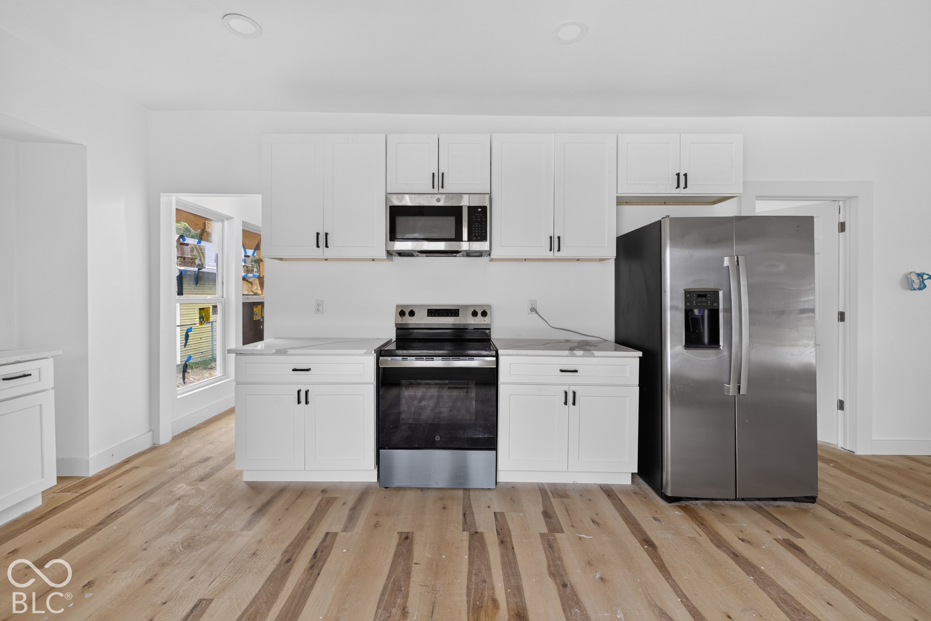 Kitchen featuring stainless steel appliances, white cabinetry, light countertops, and wood-finish flooring