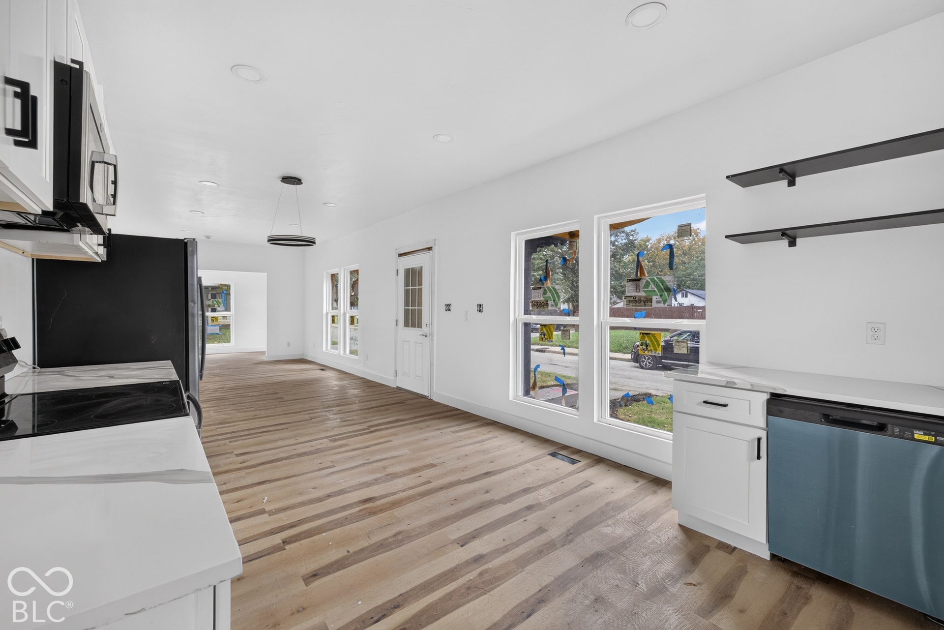 Wood-finish flooring, white cabinetry with dark hardware, sleek black floating shelves, and a stainless steel dishwasher