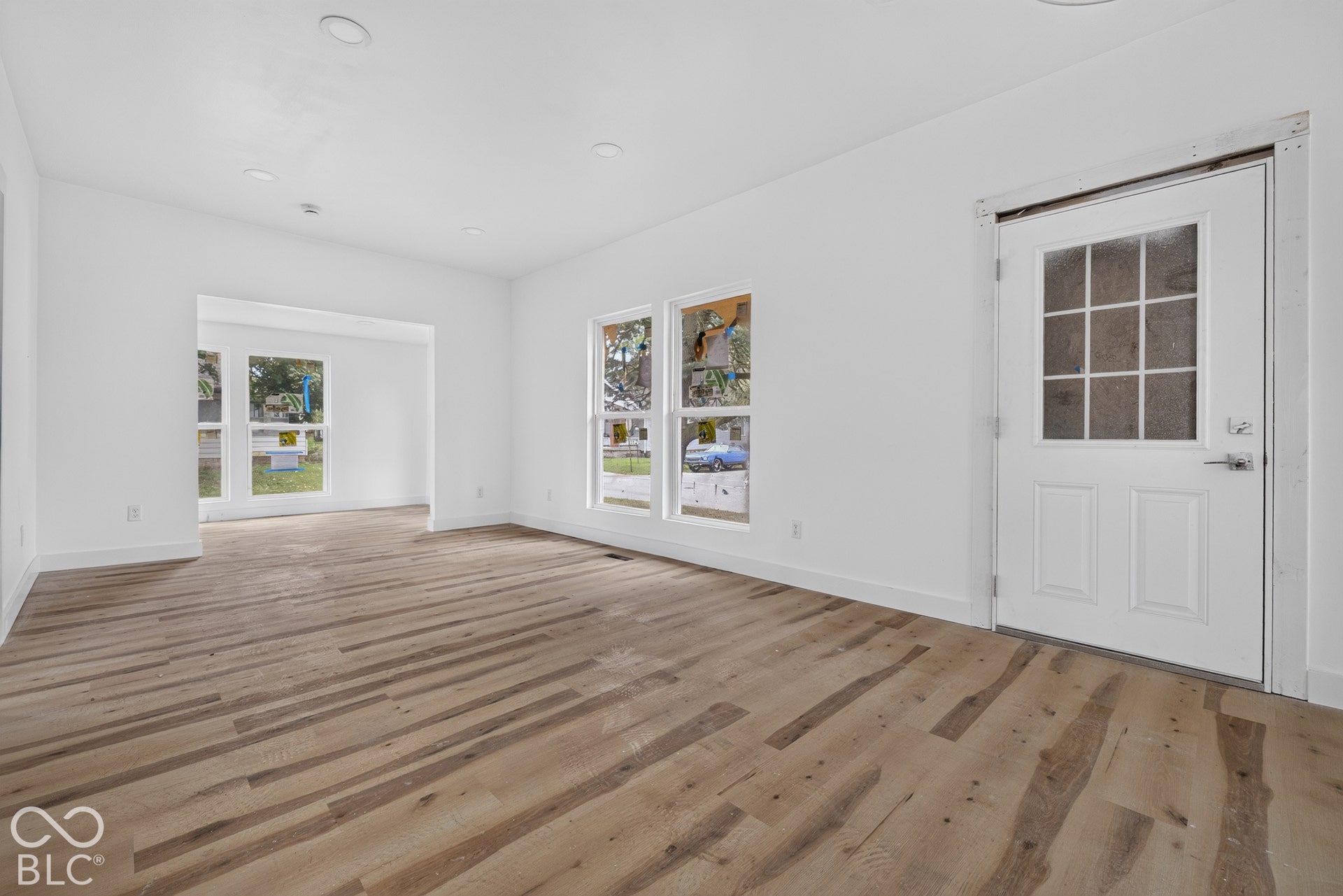 Wood-finish flooring, multiple windows, recessed lighting, white walls, and a white paneled door with glass inserts