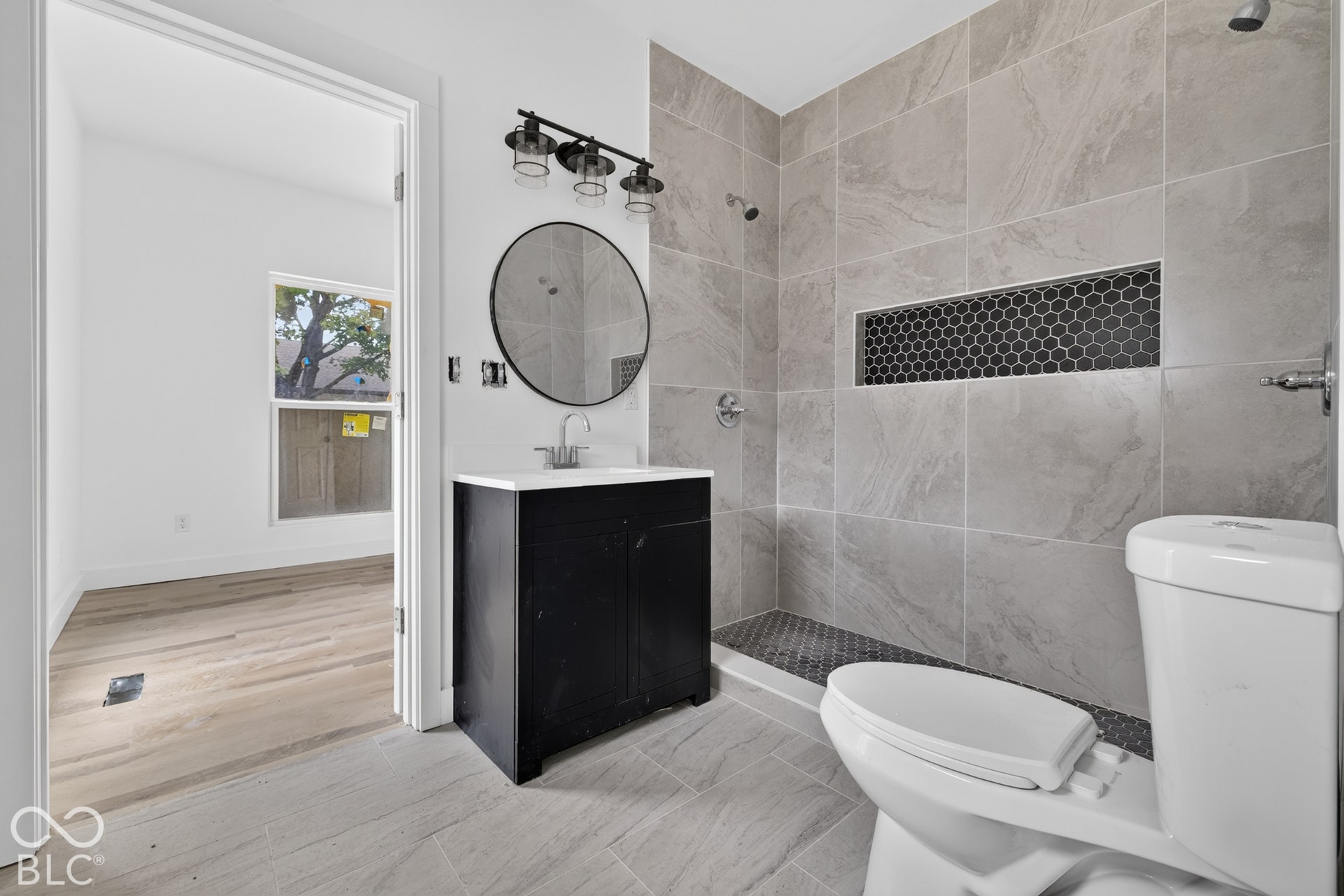 Dark wood-finish vanity with a white countertop, round mirror, and black three-light fixture