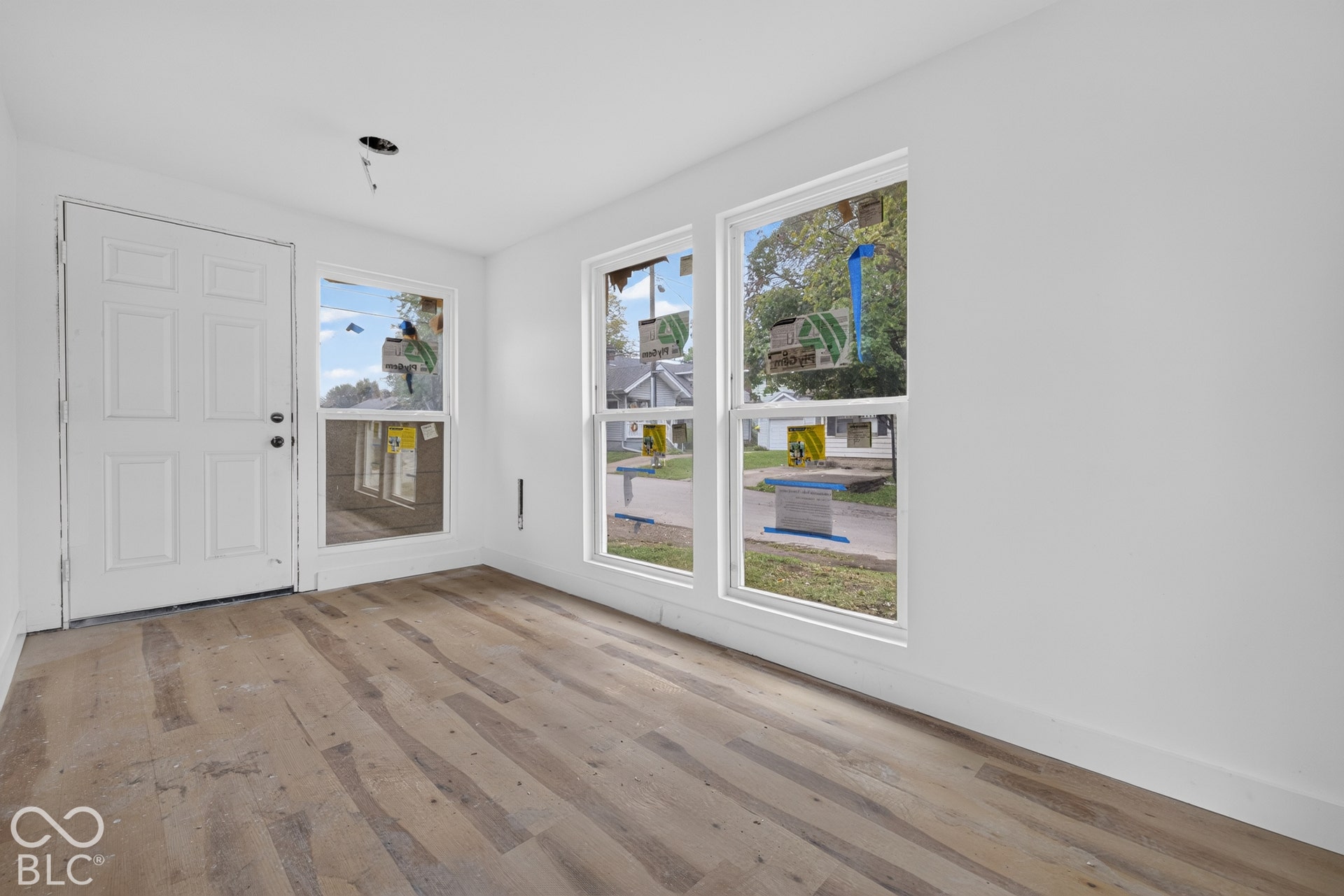 White paneled entry door, two large windows, wood-finish flooring, and white painted walls