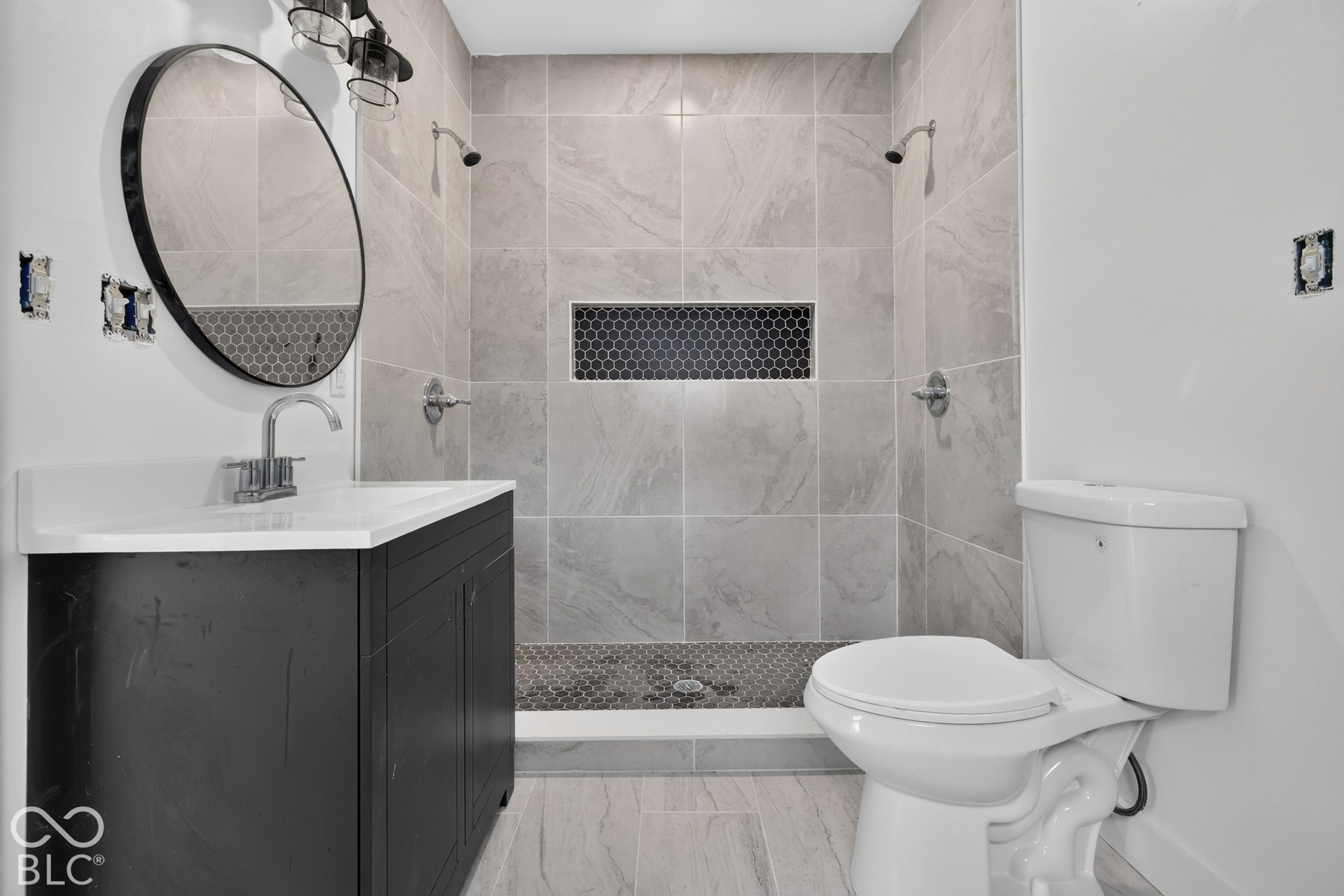 Walk-in shower with light-toned wall tile, dark hexagonal floor tile, and a recessed niche