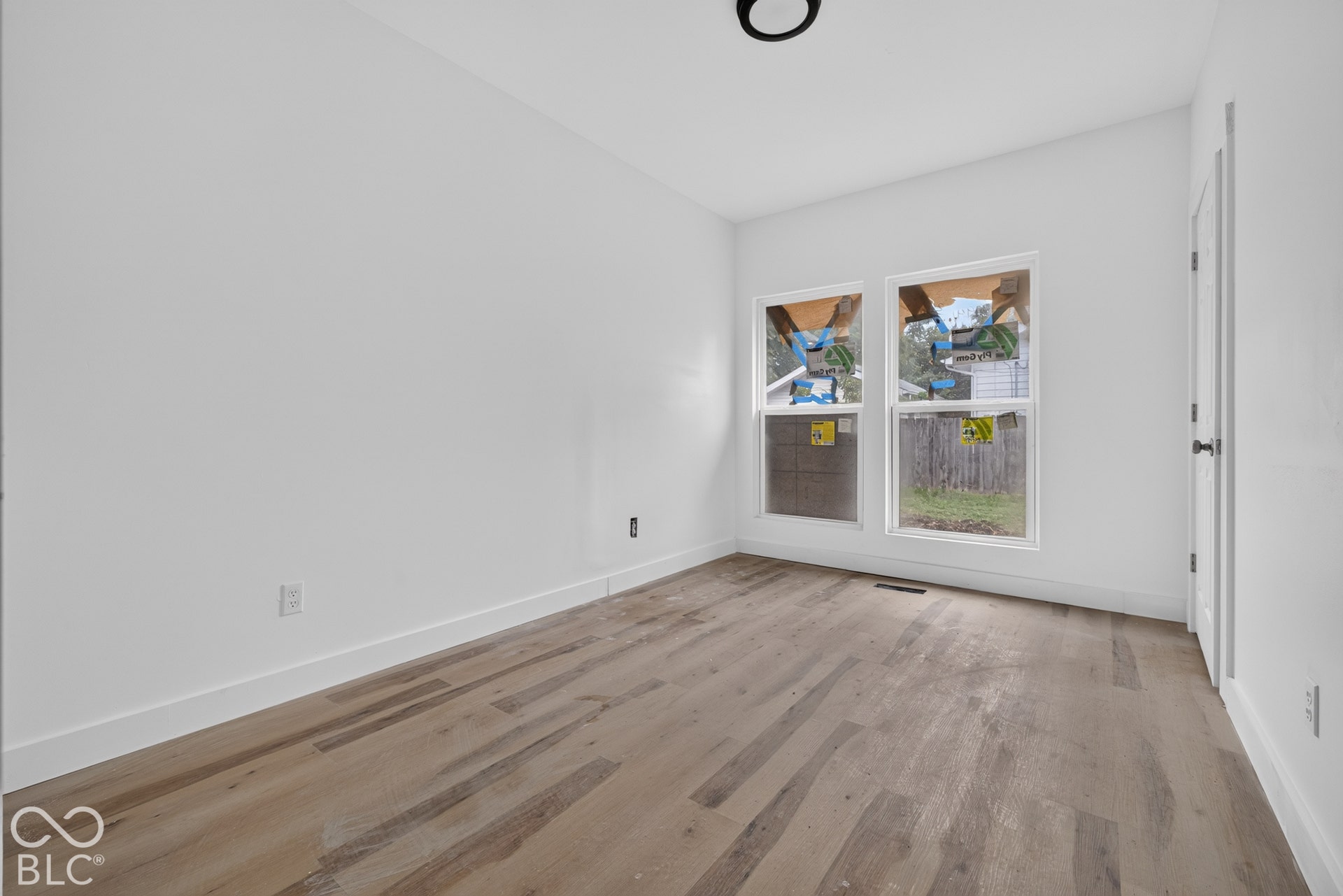 Recessed lighting, light wood-finish flooring, two large windows, white walls, and a white paneled door