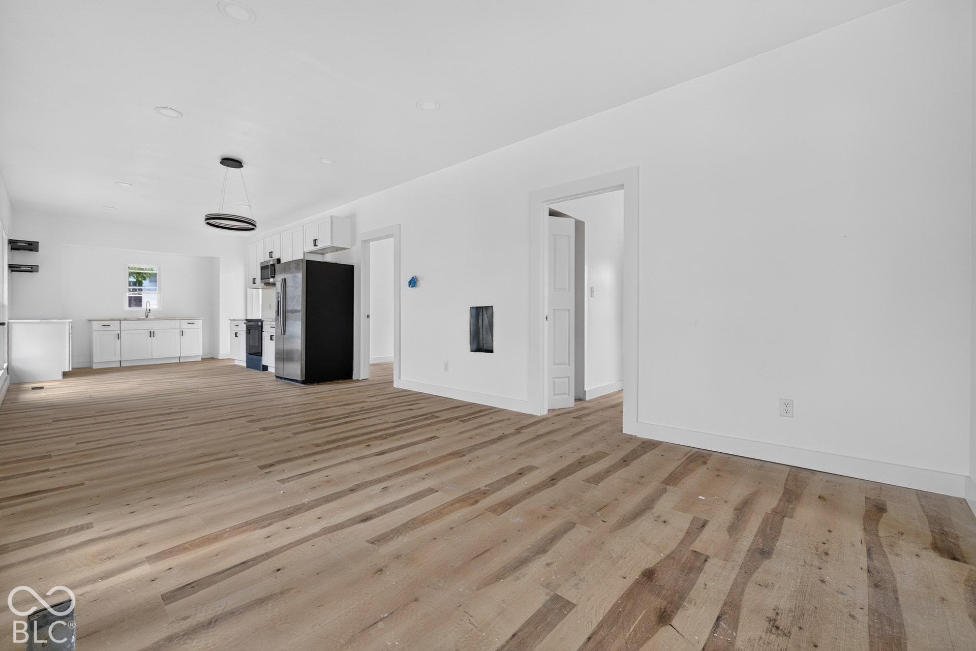 Open-concept living area with wood-finish flooring, white walls, and a contemporary pendant light fixture