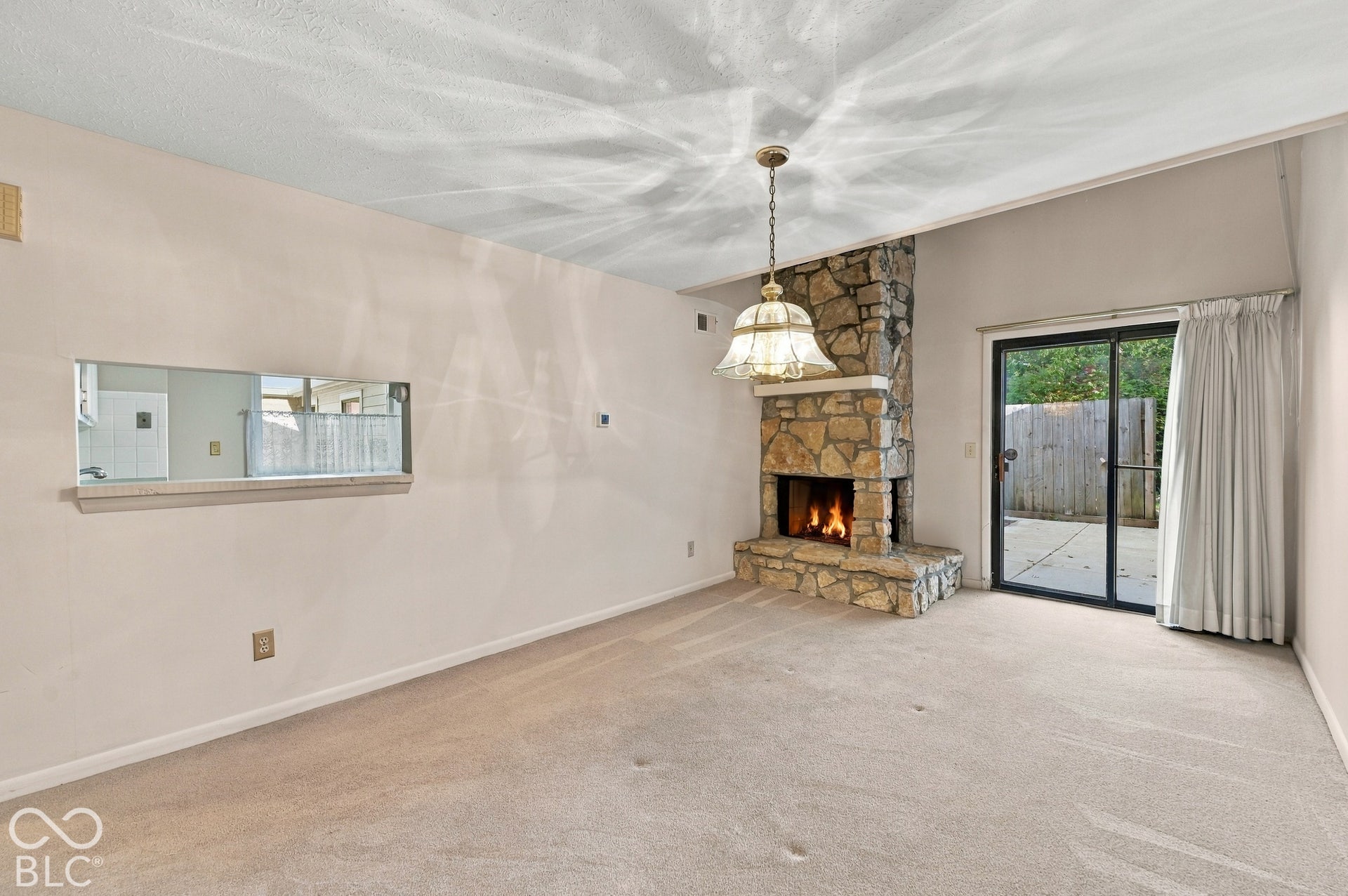 Stone-clad fireplace, sliding glass door to an outdoor patio, pass-through window, and vaulted ceiling with a pendant light fixture