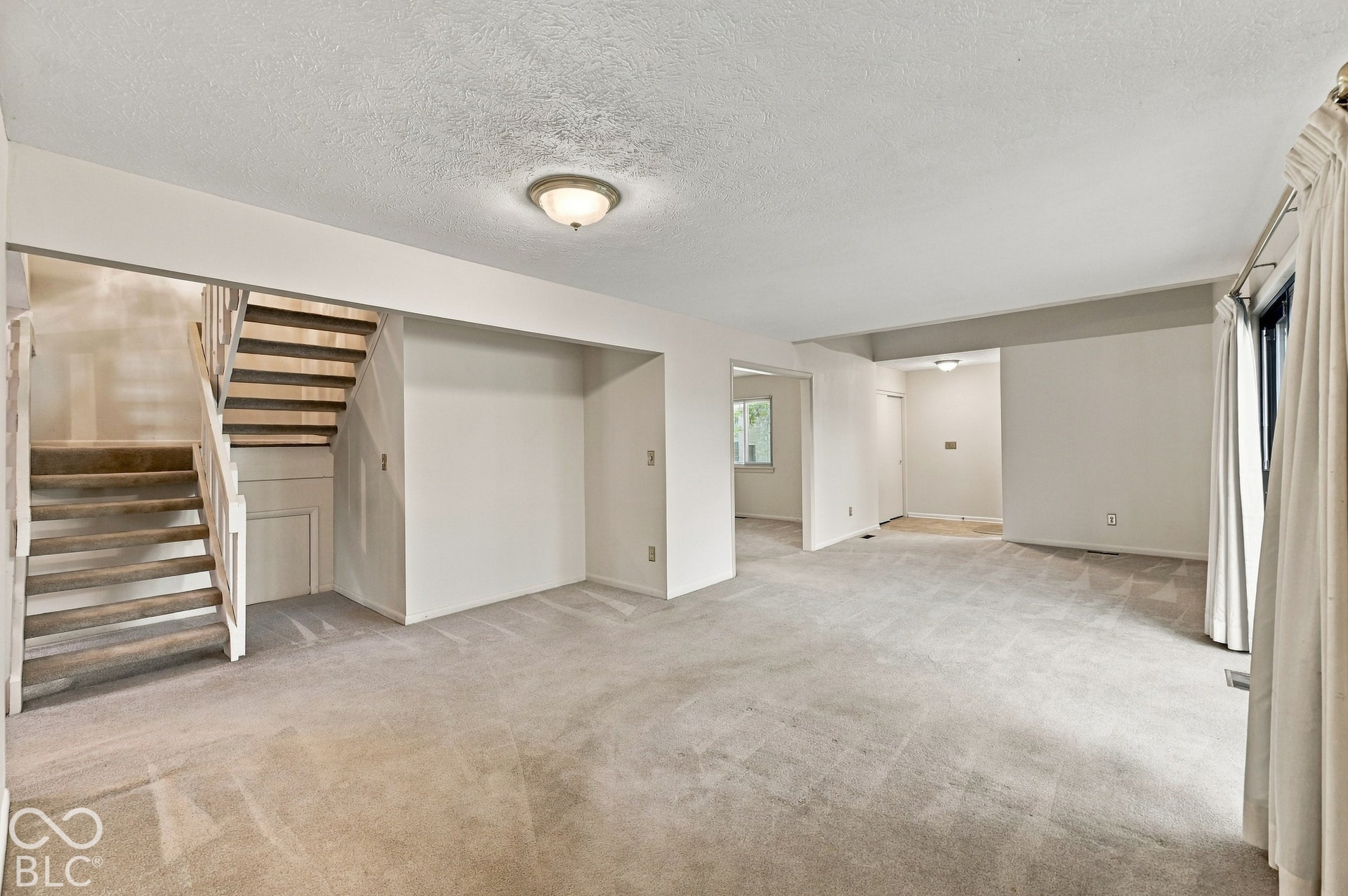 Expansive carpeted area with a staircase featuring wood-finish treads and white risers