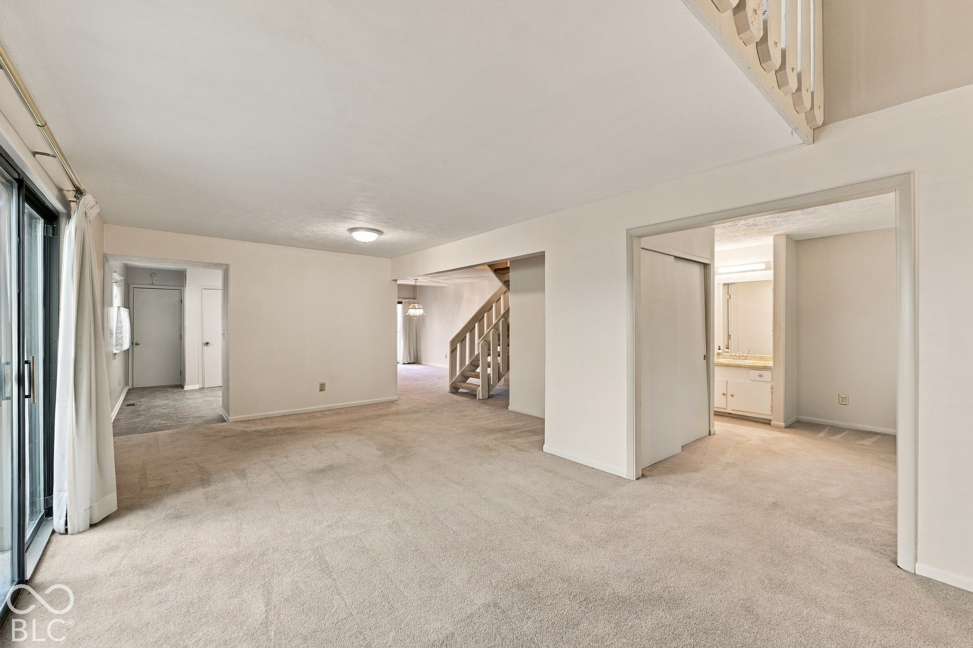 Open-concept living space with light-toned carpeting, a sliding glass door, and a built-in staircase with wood railings