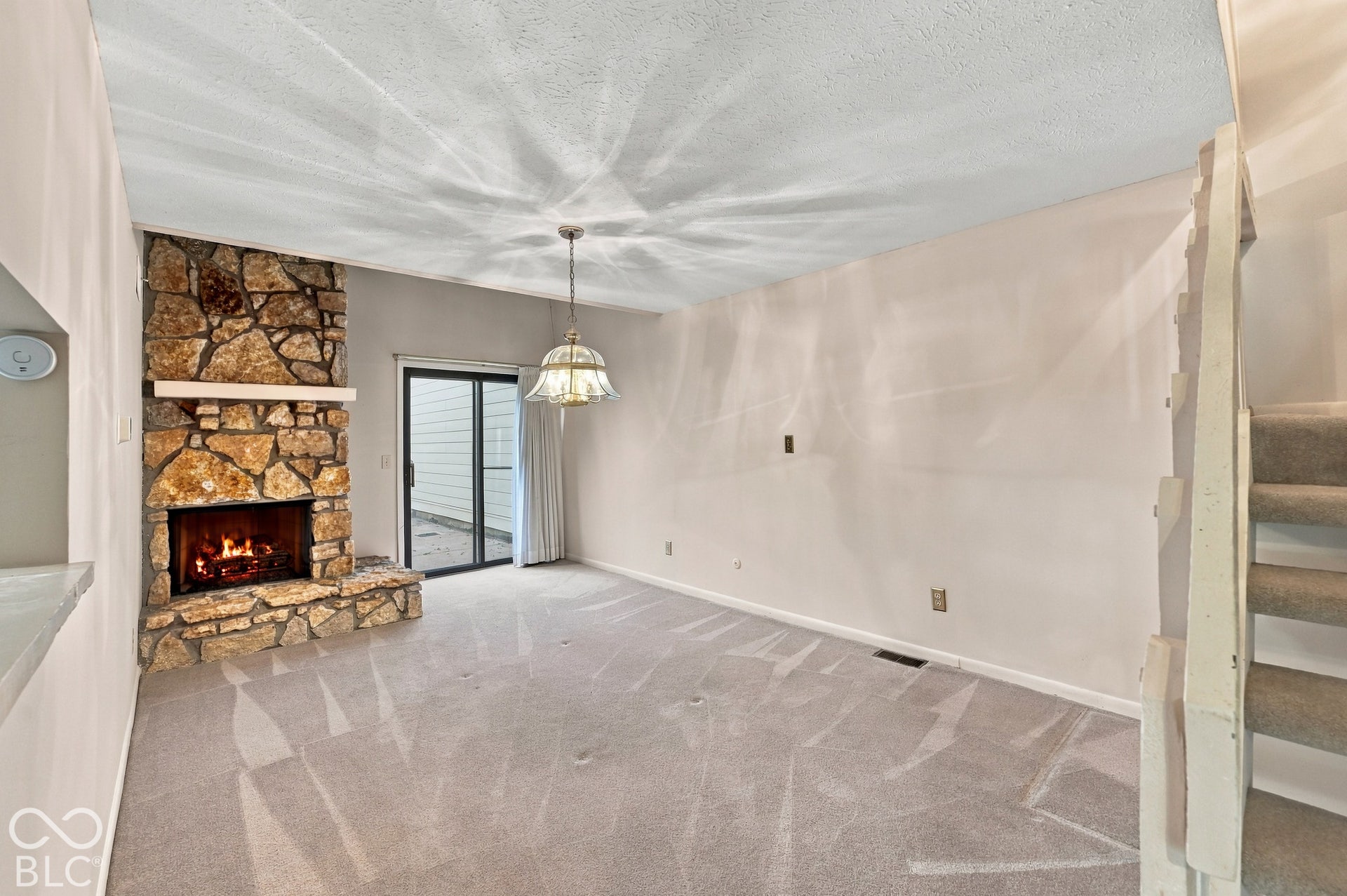 Stone-clad fireplace with a hearth, sliding glass door, pendant light fixture, and carpeted flooring