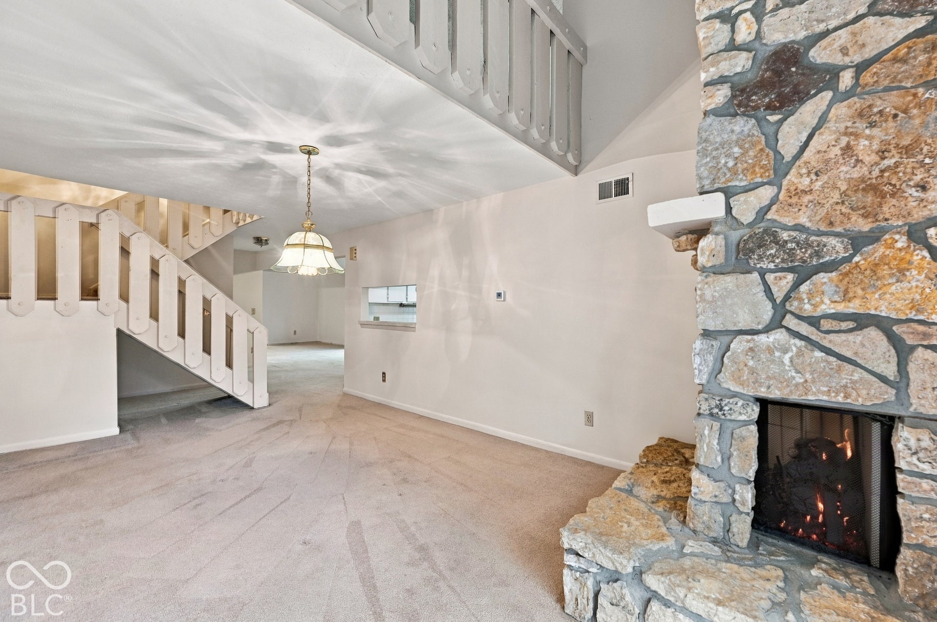 Stone fireplace with a hearth, carpeted flooring, and a two-story ceiling