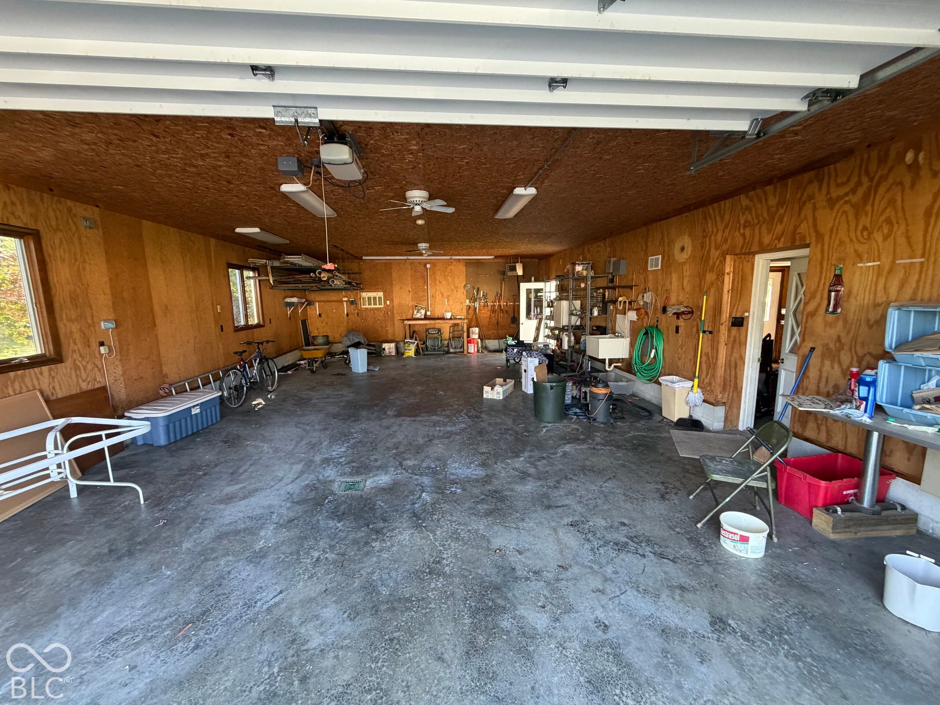 Spacious garage featuring concrete flooring, wood-paneled walls, multiple windows, built-in lighting, and ceiling fans