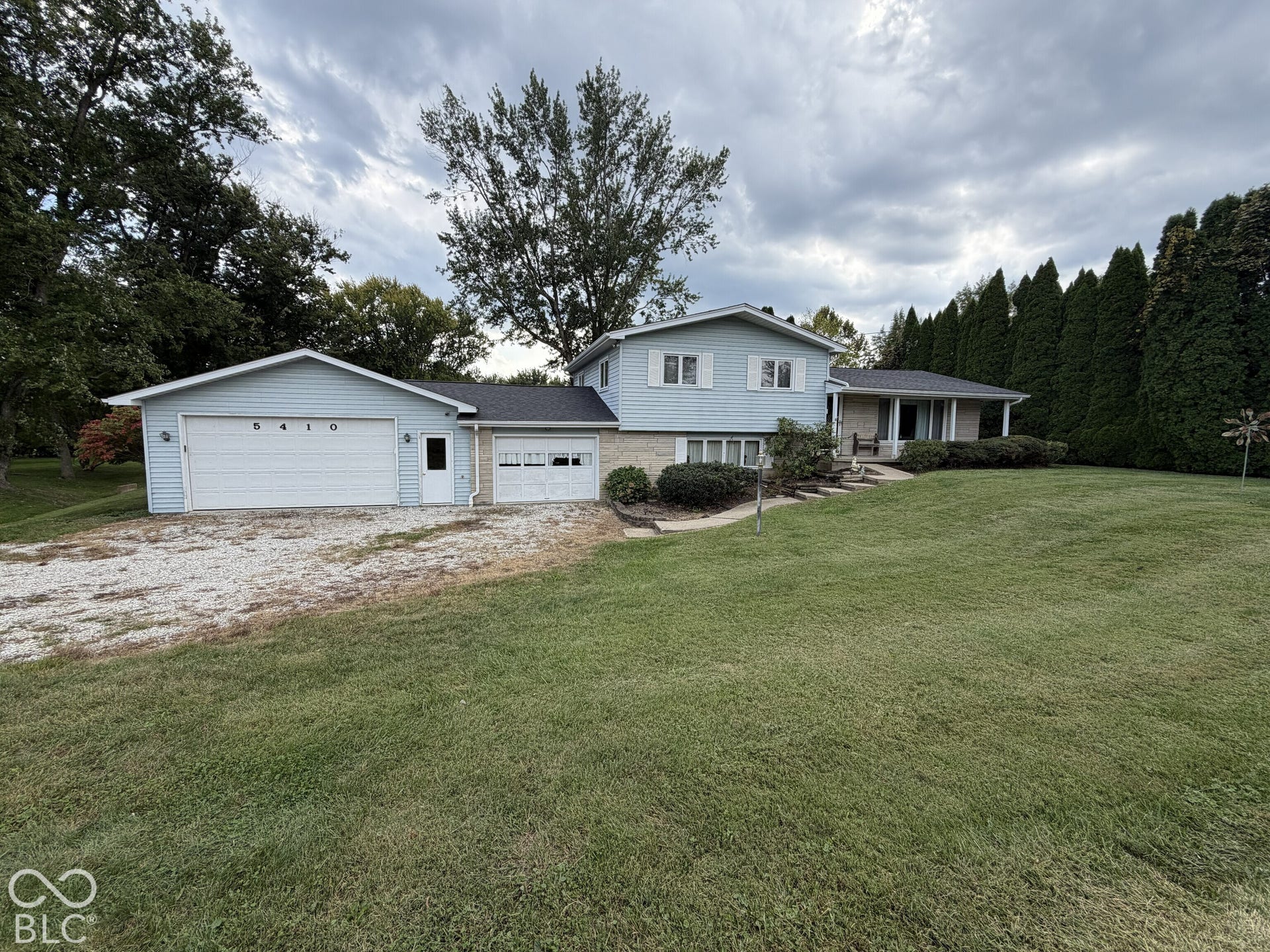 Exterior featuring light blue siding, white trim, stone accents, two attached garages, and a covered front entry