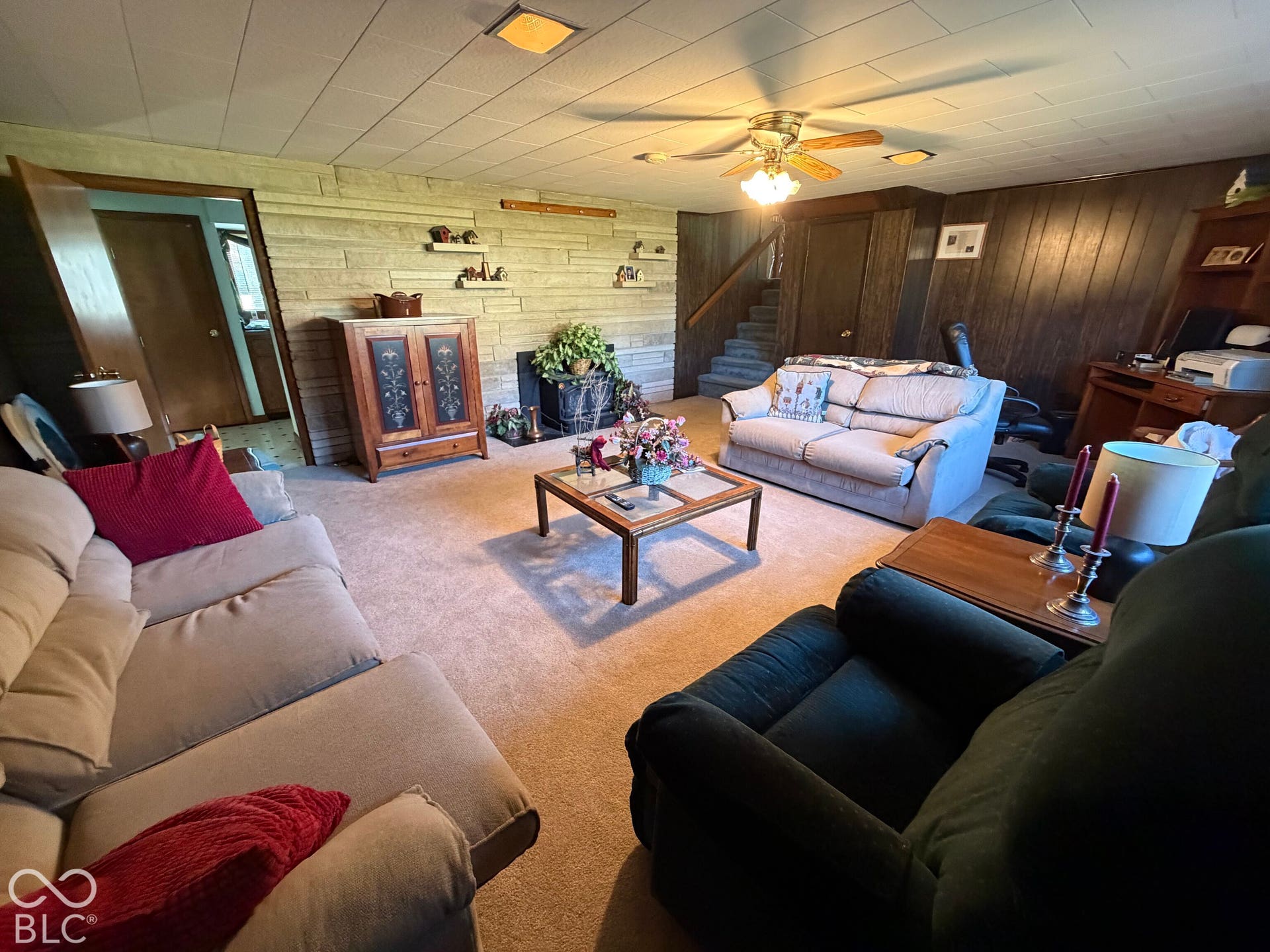 Carpeted living area featuring a stone accent wall, wood paneling, and a ceiling fan with integrated lighting