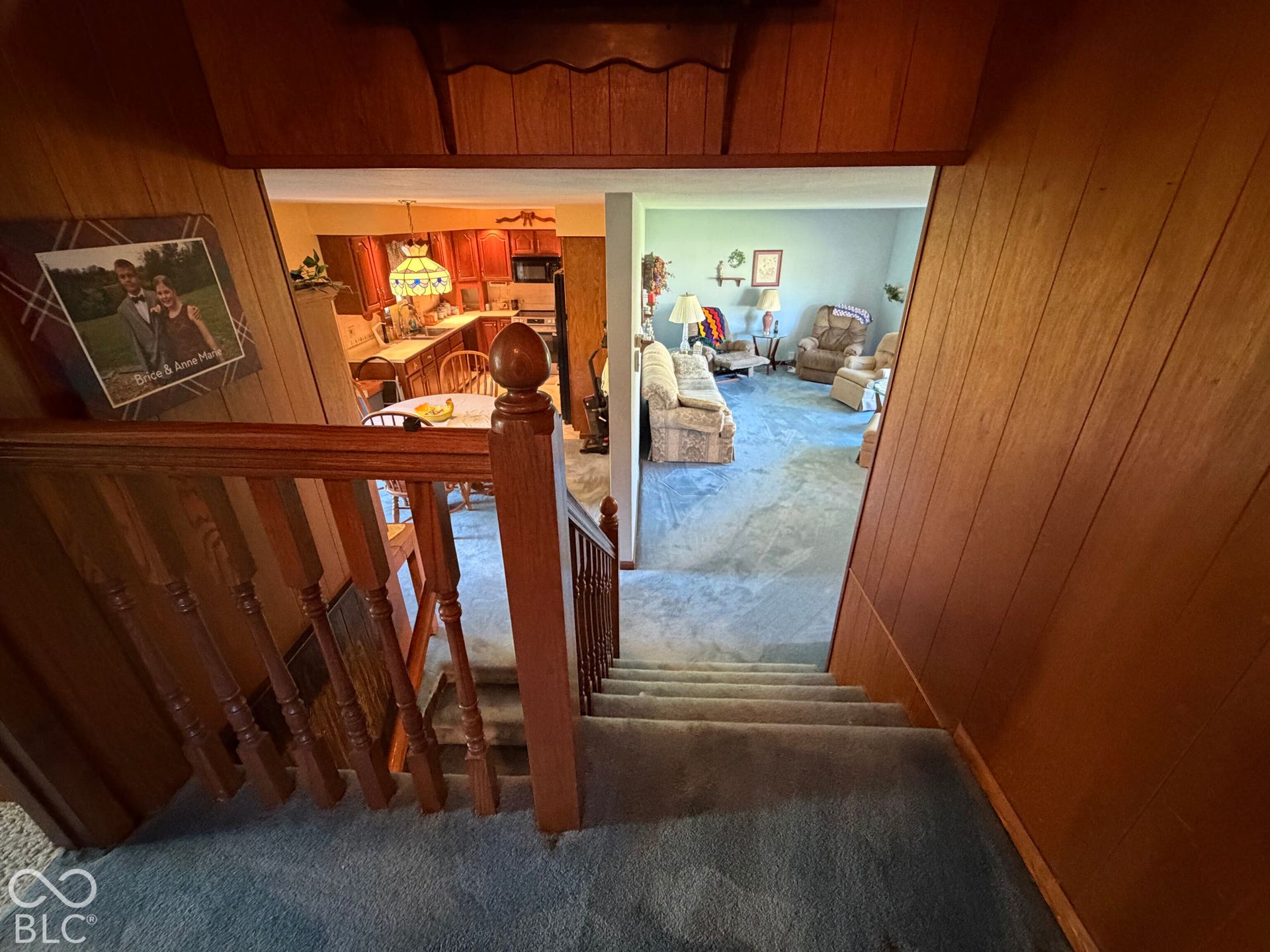 Wood paneling throughout the stairwell, carpeted stairs, and a wood banister with ornate newel post