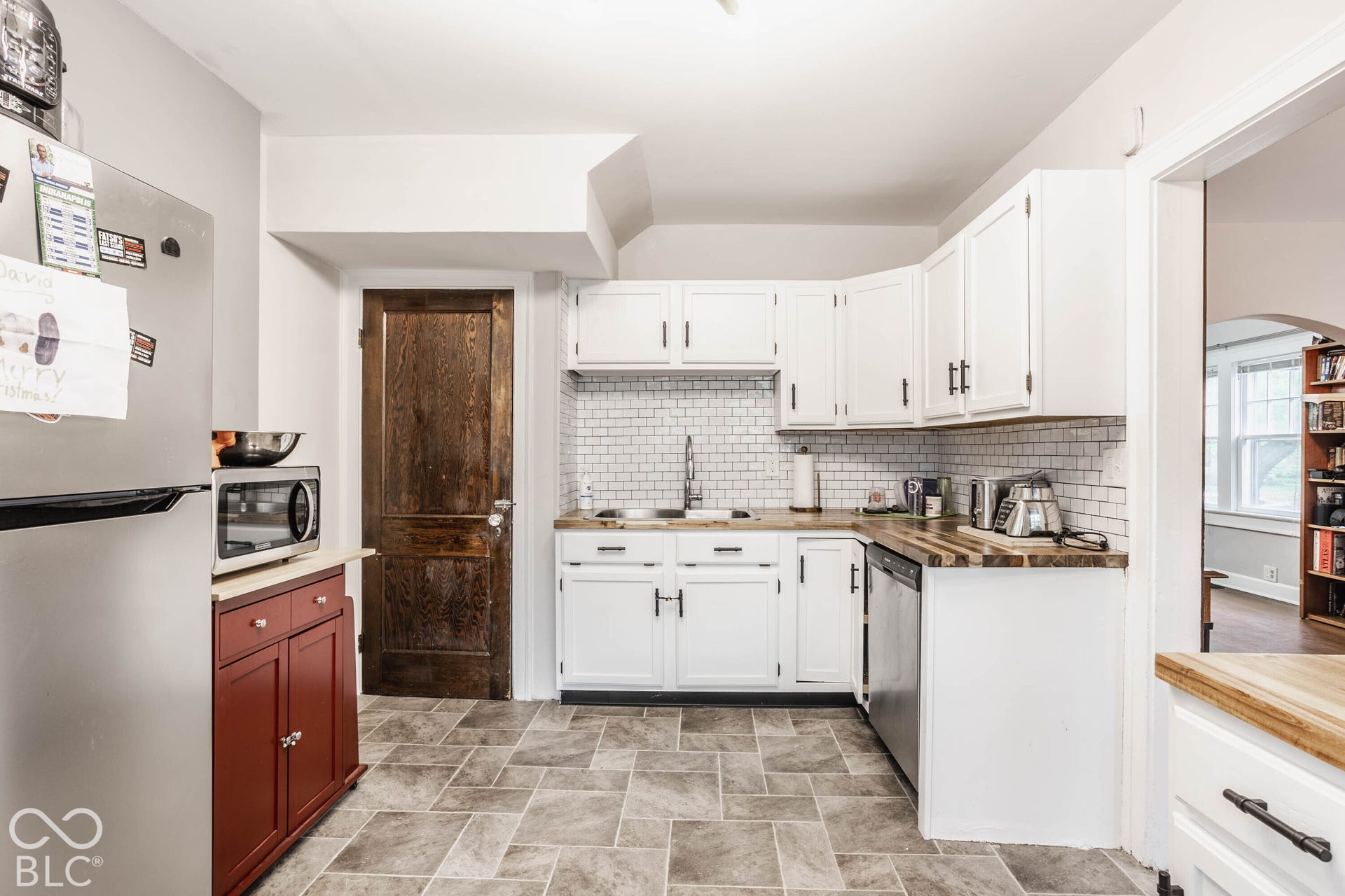 White cabinetry with dark hardware, subway tile backsplash, wood-finish countertops, stainless steel sink, and patterned floor tiling