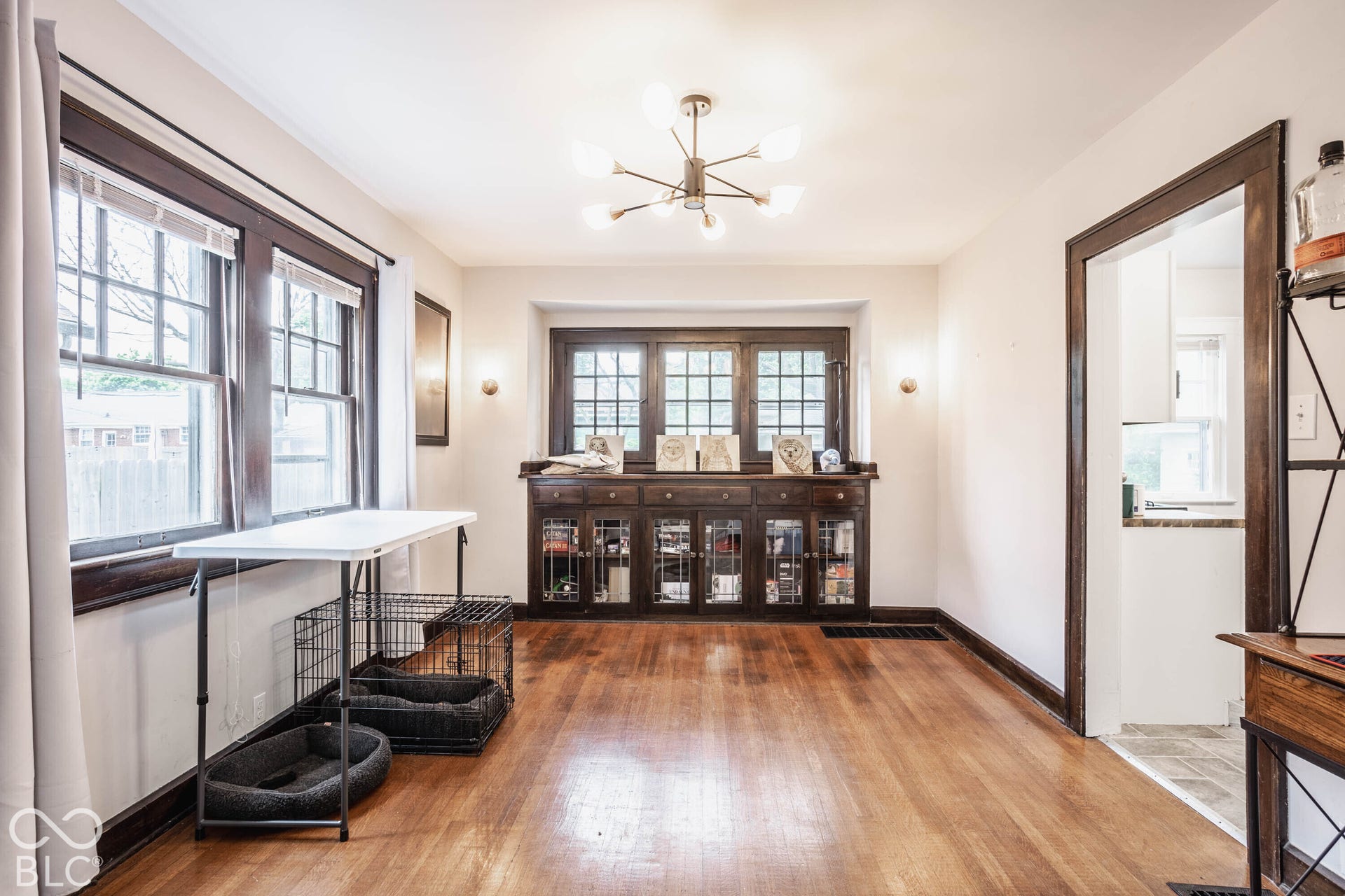 Hardwood flooring, dark wood trim throughout, built-in cabinetry with glass-front doors, recessed window with multiple panes, and a modern ceiling fixture