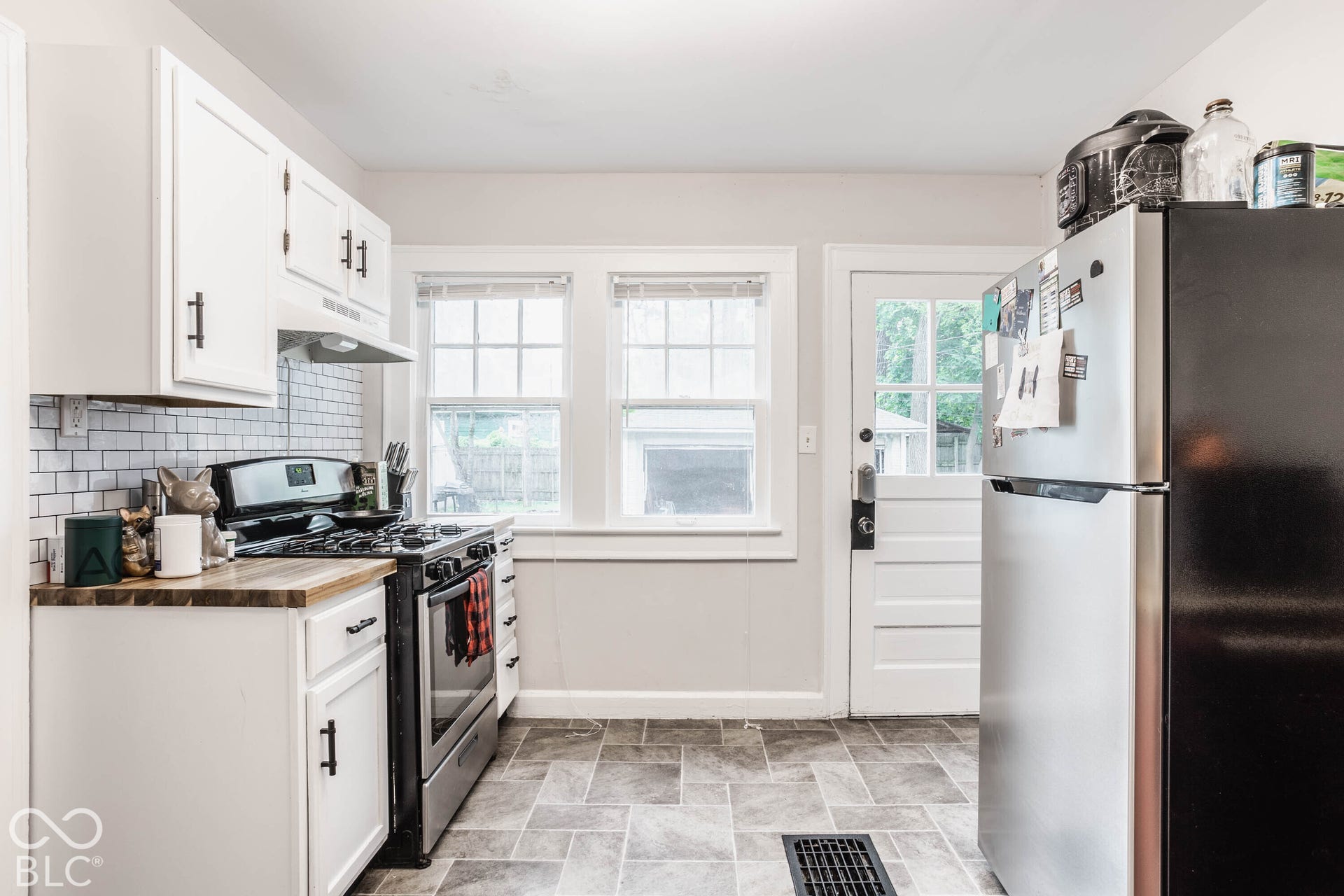 White cabinetry with matte black hardware, wood-finish countertops, subway tile backsplash, stainless steel gas range, and two double-hung windows