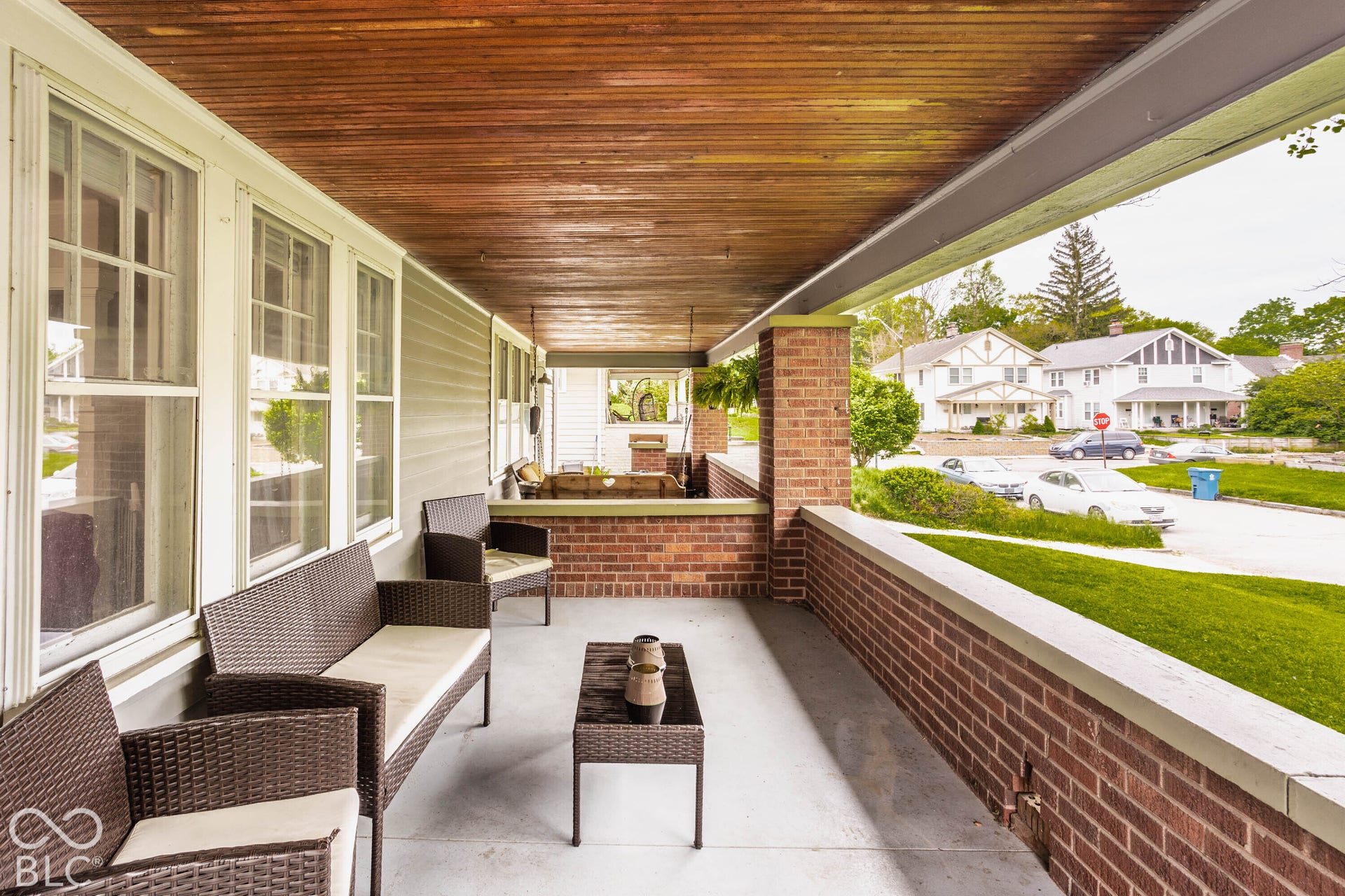 Covered front porch featuring a wood-finish ceiling, brick support columns, brick half-walls, and multiple double-hung windows