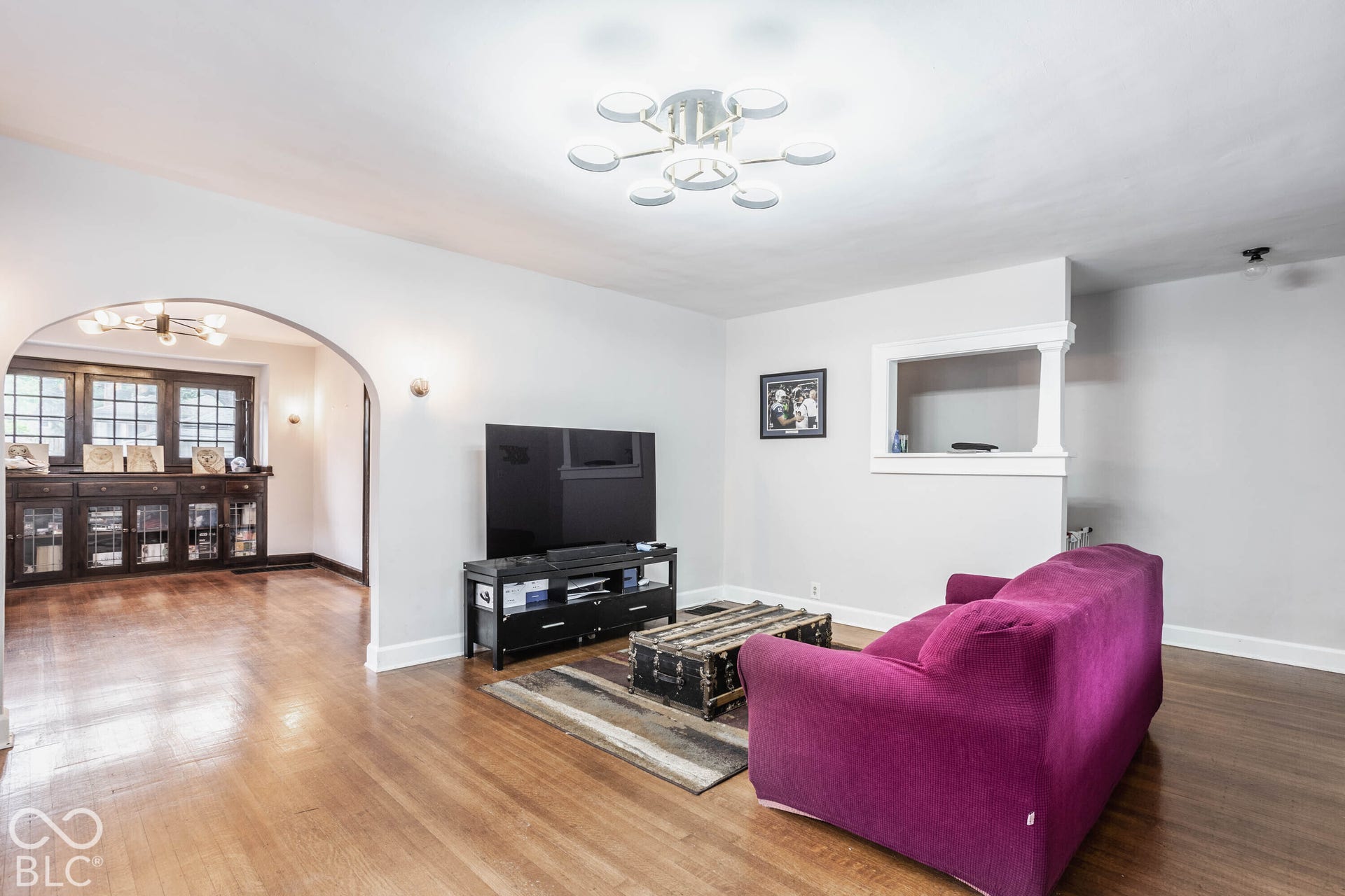 Hardwood flooring throughout, arched doorway, built-in shelving, decorative window trim, and a contemporary ceiling fixture