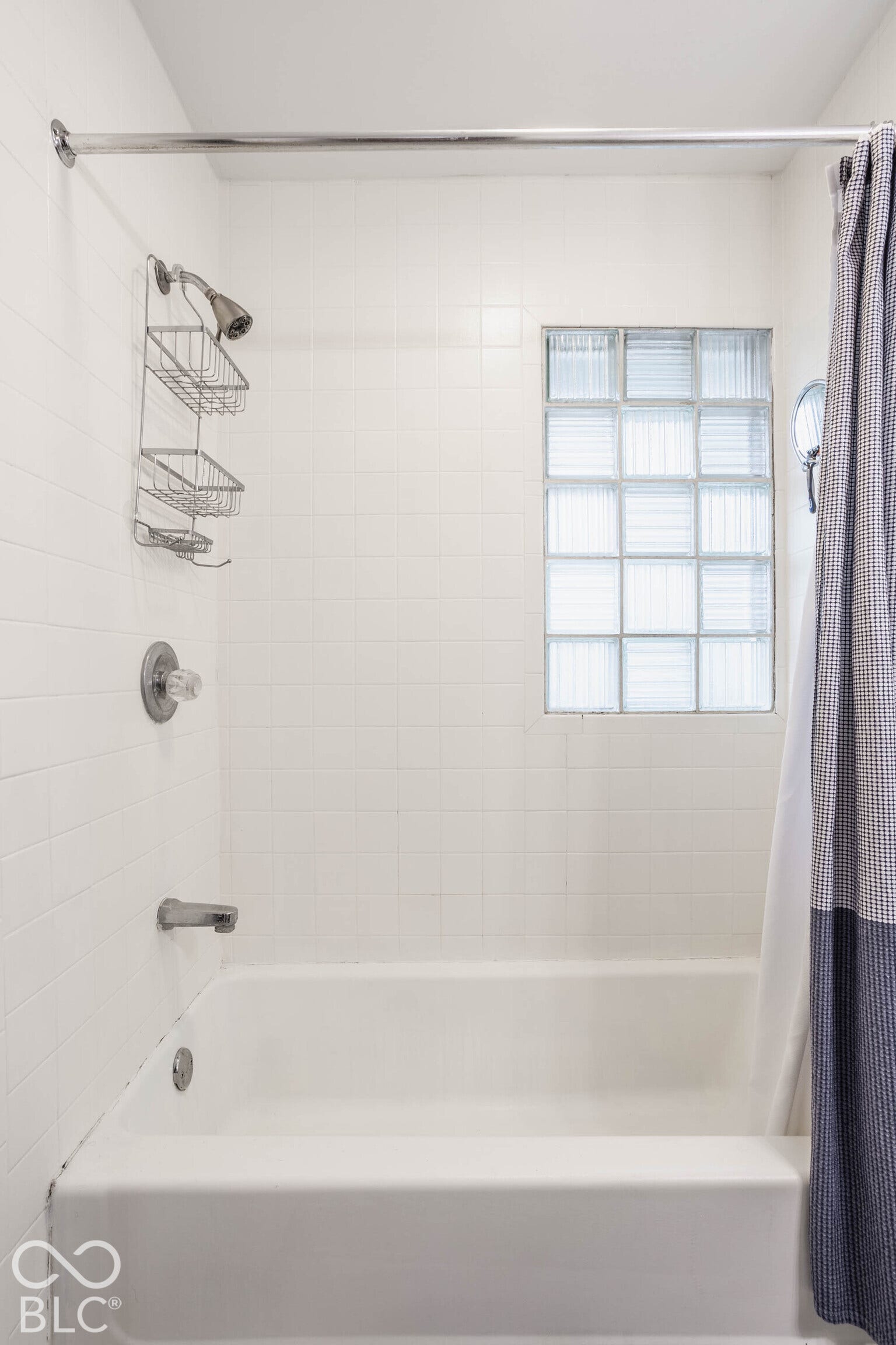 Bathtub with white tile surround, glass block window, and chrome fixtures
