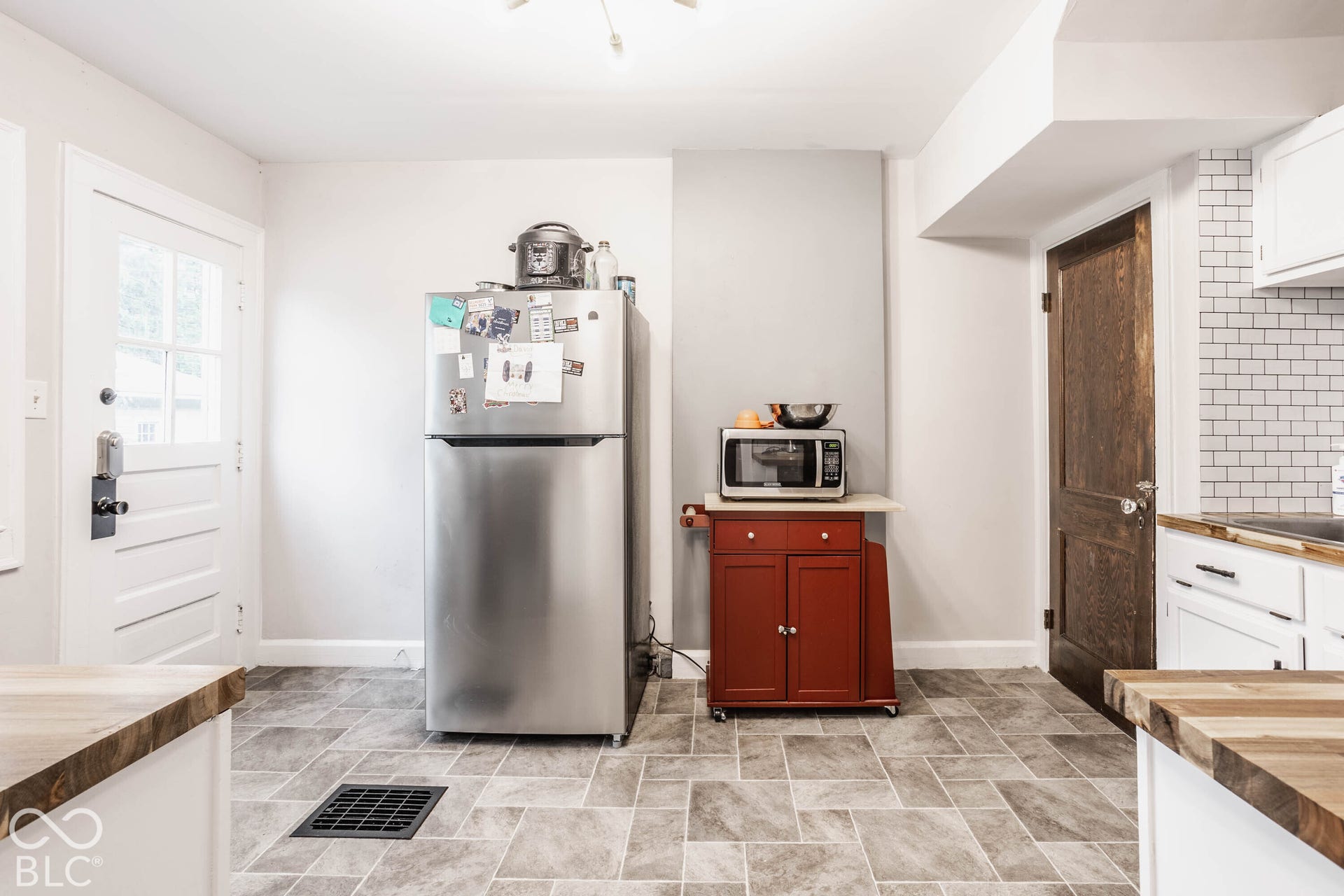 Kitchen featuring tile flooring, white subway tile backsplash, white cabinetry, and wood-finish countertops