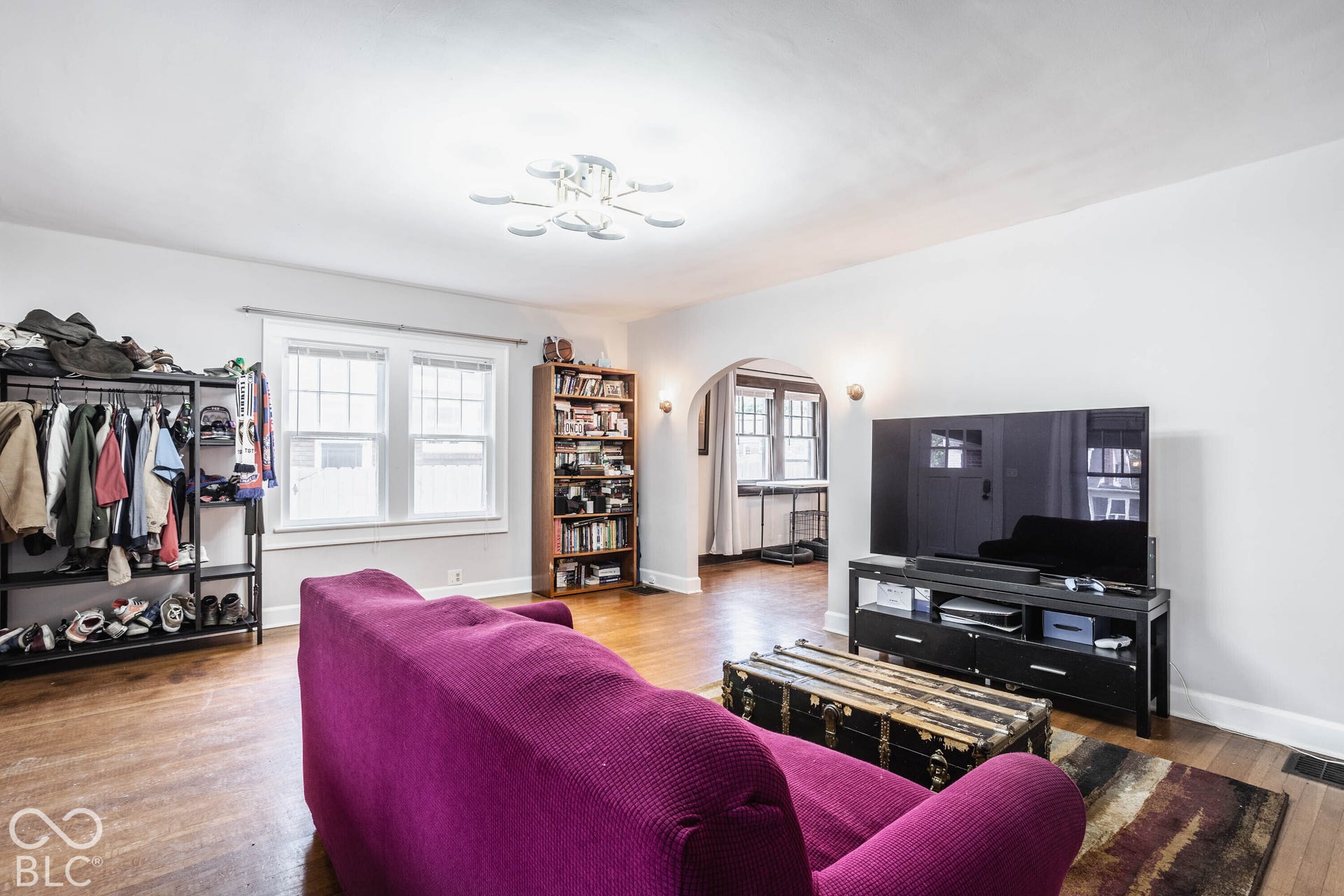 Bright living room showcasing hardwood flooring, a large picture window with natural light, built-in shelving with storage, and a black media console with integrated entertainment cabinetry