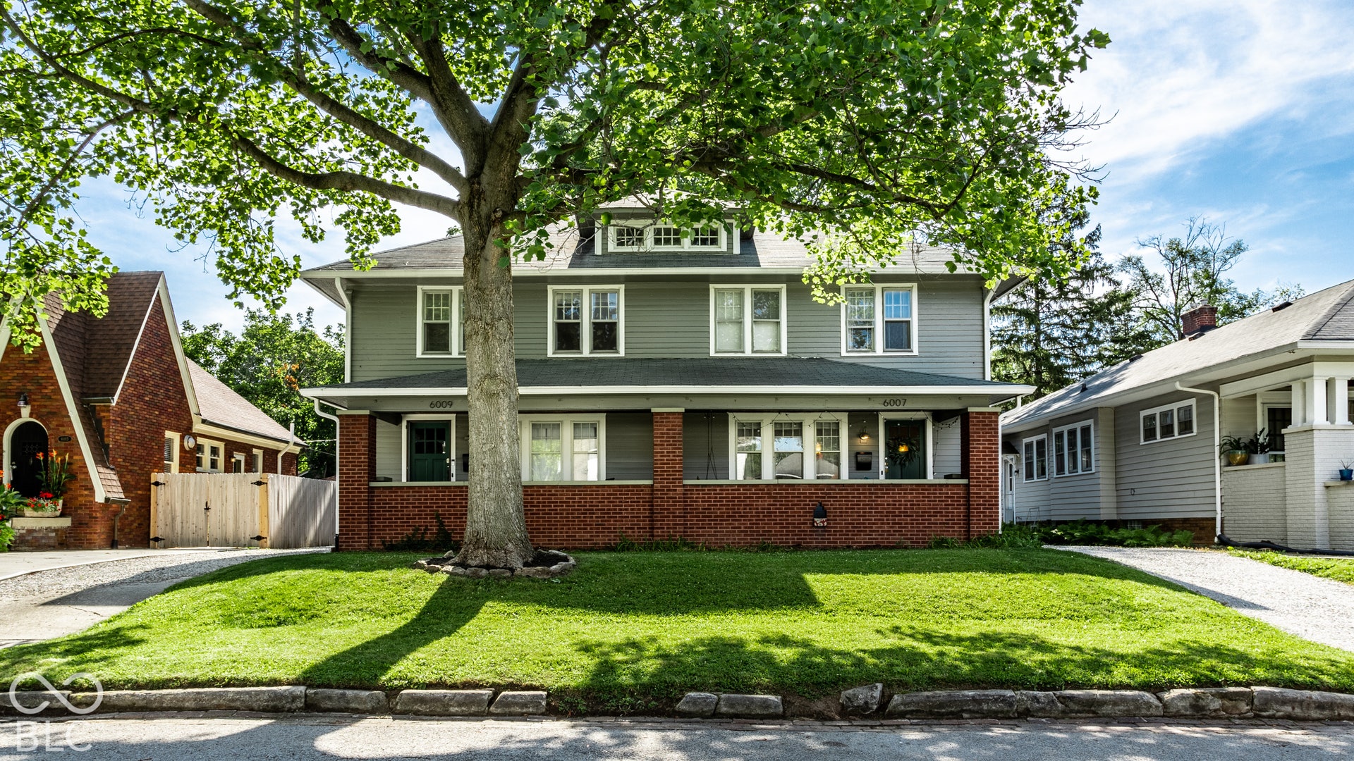 Two-story residence featuring a gray exterior with white trim, brick foundation, and a prominent front lawn