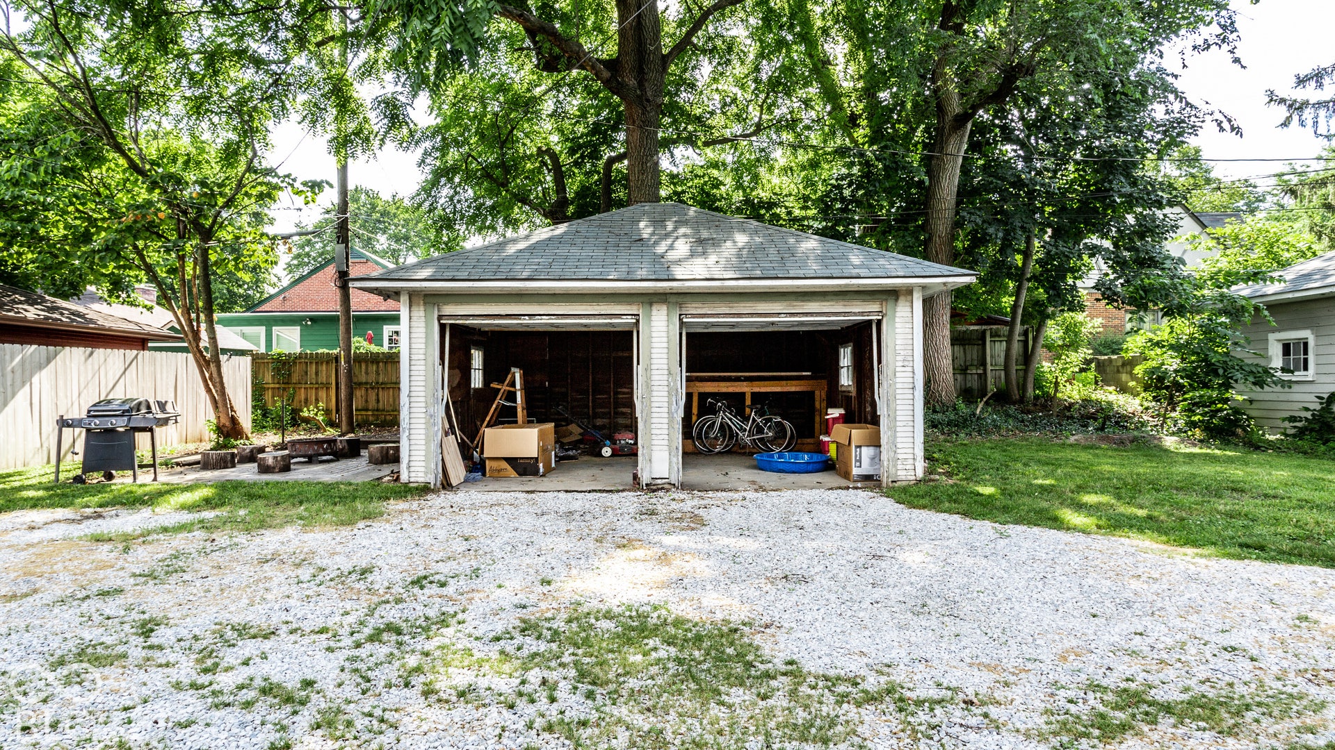 Detached two-car garage with overhead doors, gravel driveway, and mature trees