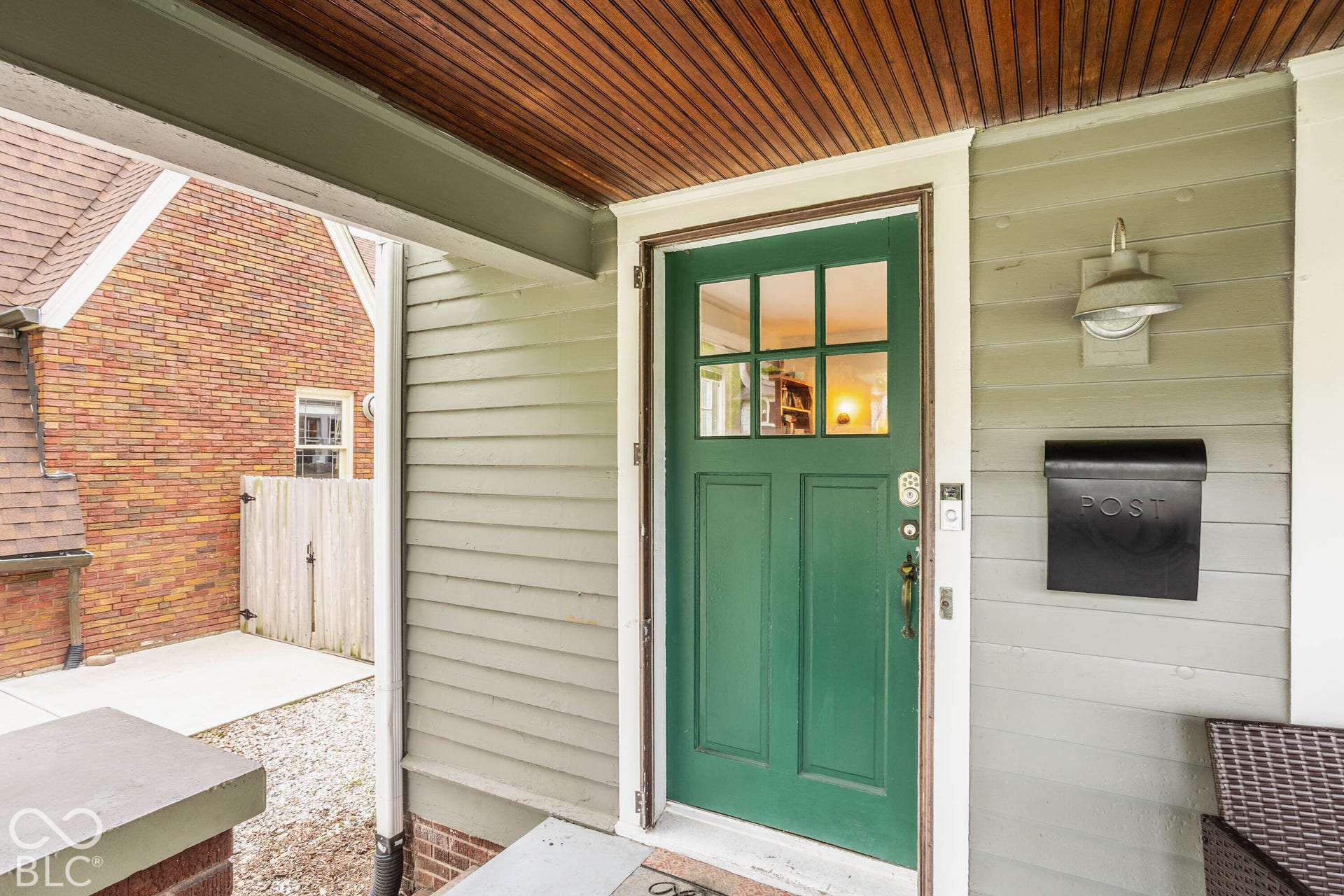 Wood-finish ceiling on porch, green six-panel door with divided lites, wall-mounted exterior light fixture, black mailbox, and light gray siding