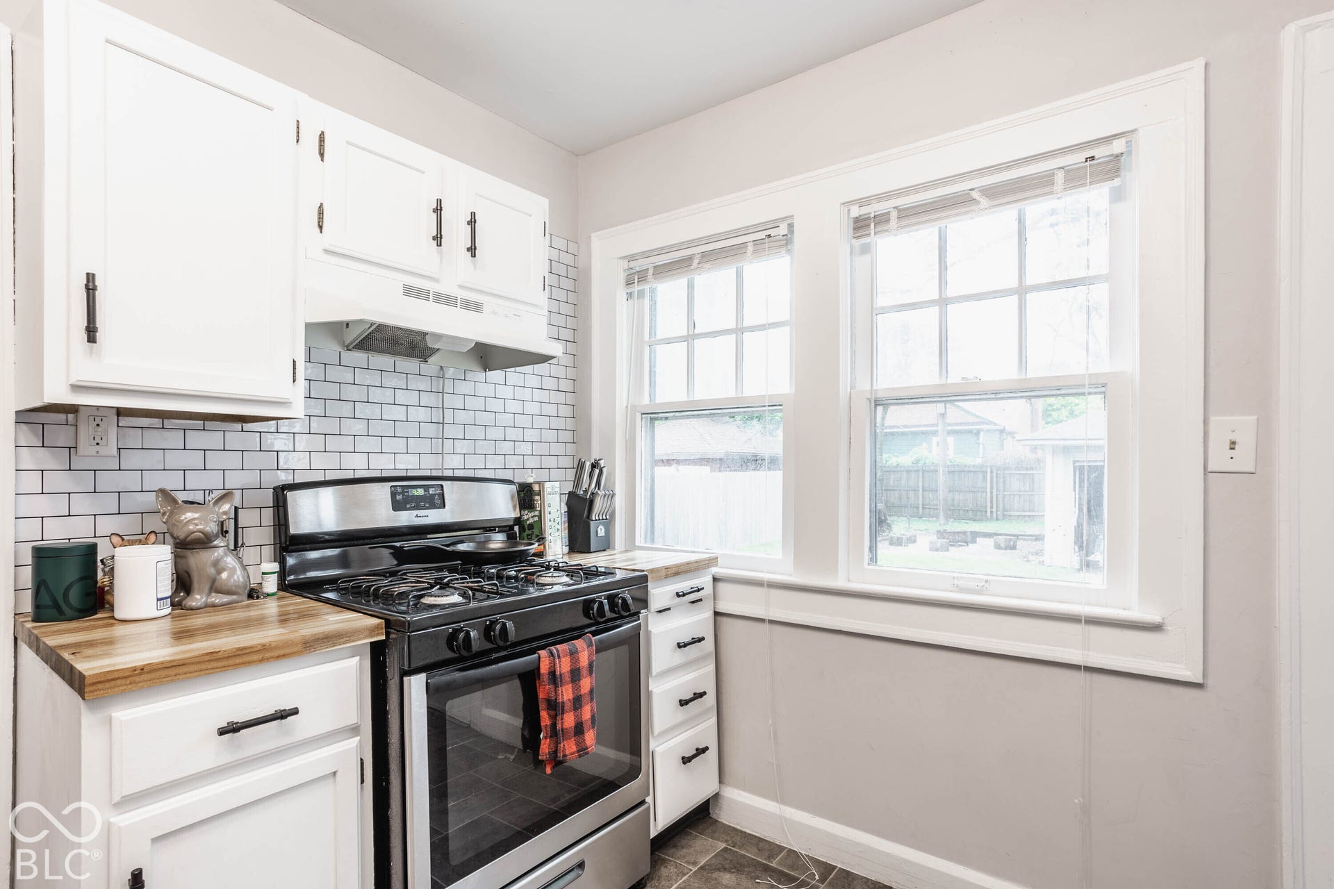 Bright, updated kitchen featuring white cabinetry with black hardware, stainless steel gas range, subway tile backsplash, and wood-finish countertops