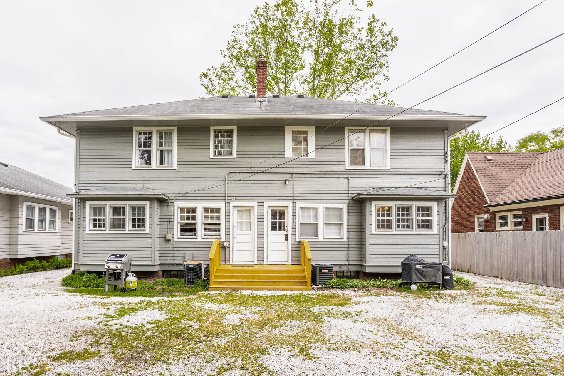 Classic two-story home featuring gray vinyl siding, multiple multi-pane windows with white trim, and a welcoming entry with bright yellow deck stairs