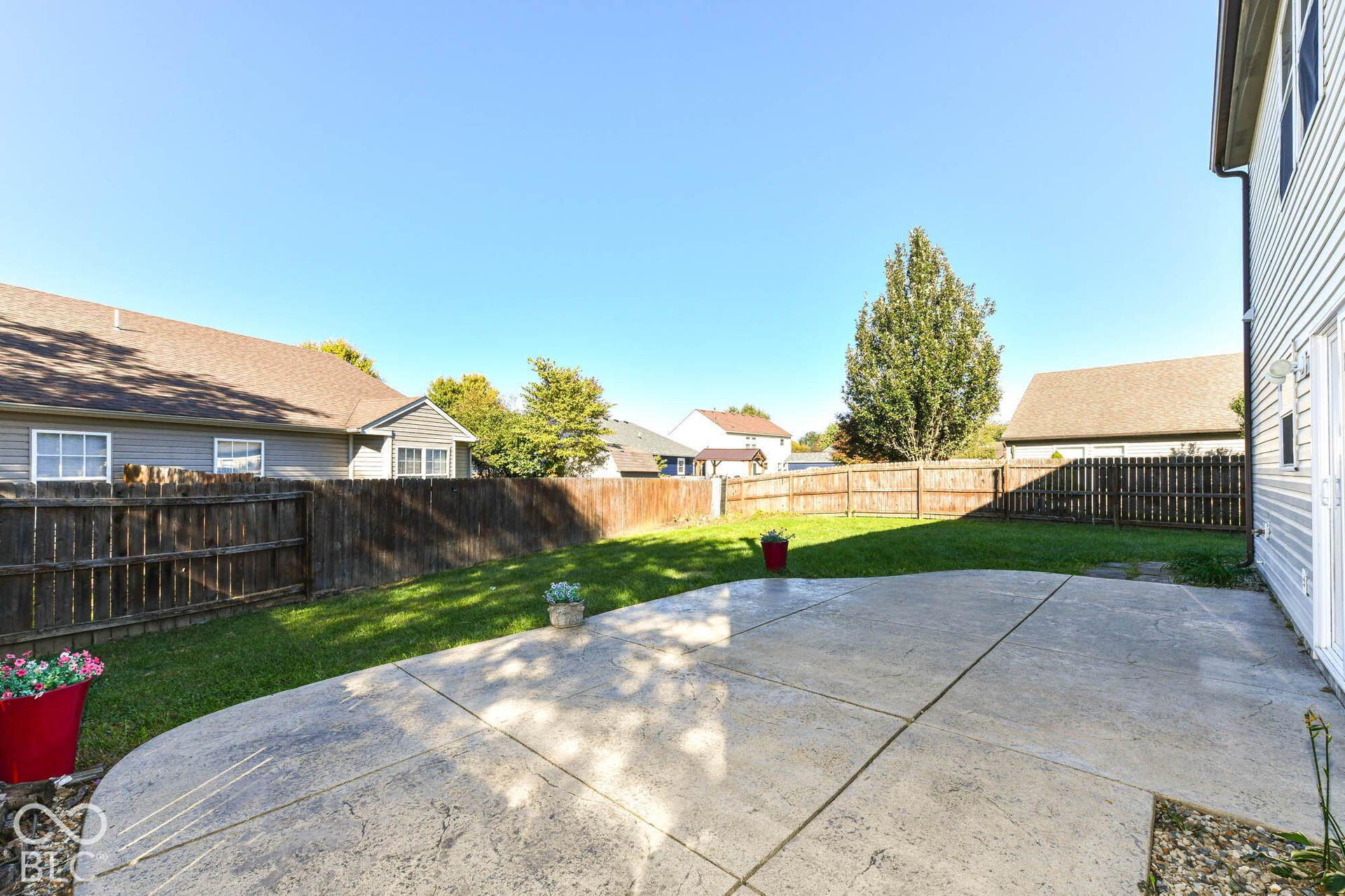 Rear patio with stamped concrete surface and an expansive lawn area, enclosed by wood fencing